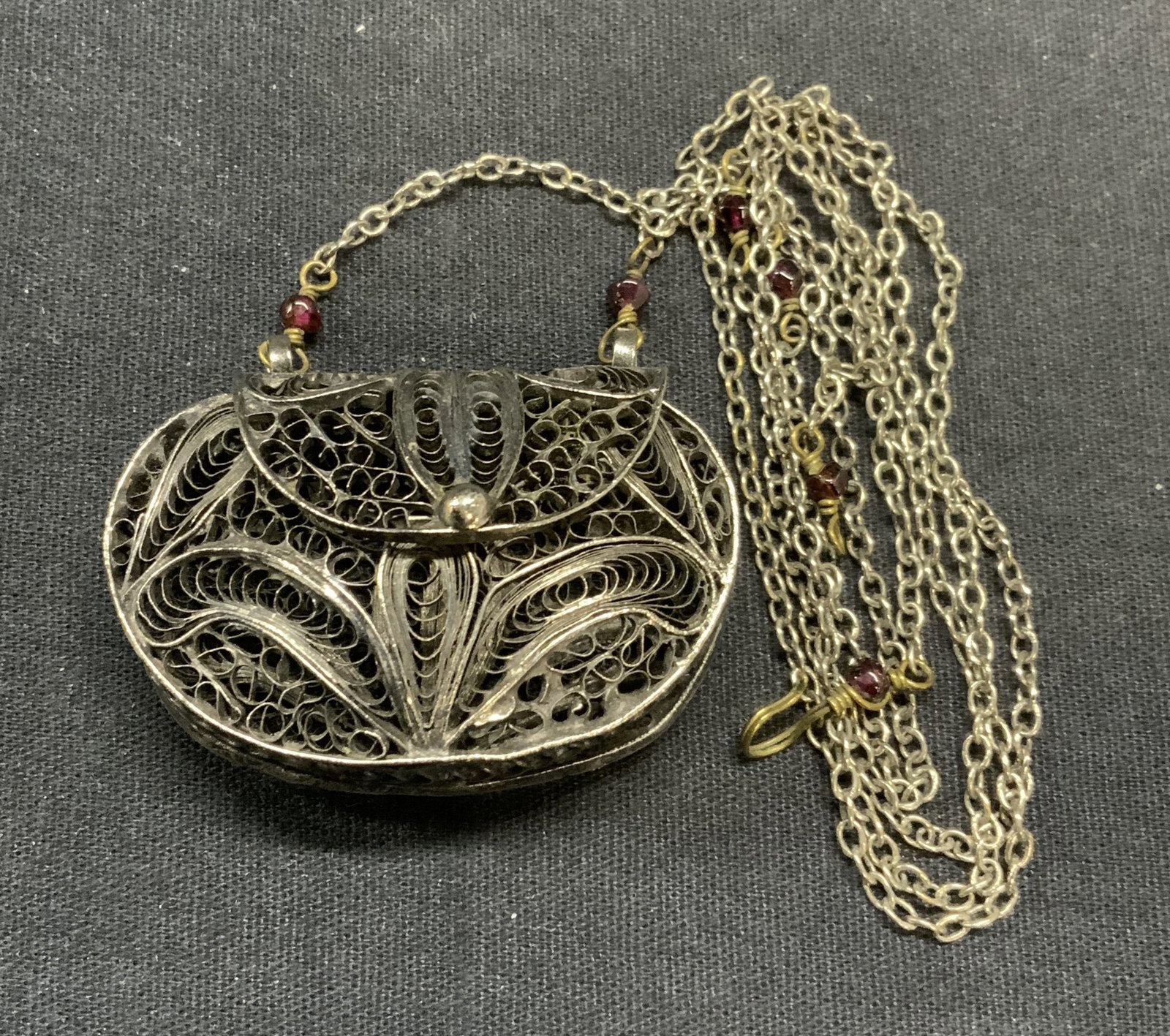 Silver Tone Purse Charm Pendant Necklace: Silver tone filigree pendant necklace with purse charm and possibly amethyst beads. Purse opens. Drop length approx. 16 inches. Pendant measures approx. 1.25 x 1 7/8 inches. Some scratching observed. 