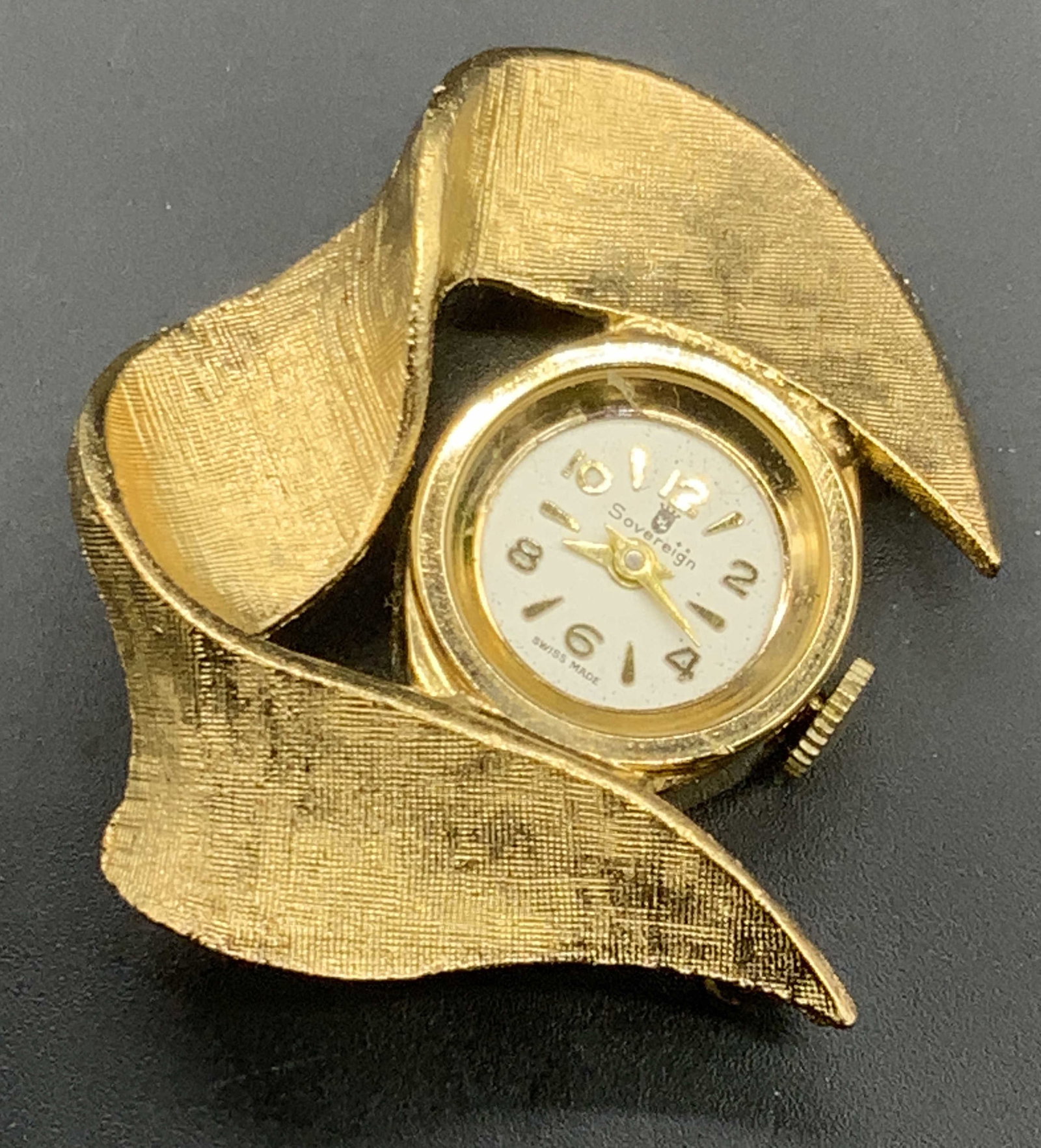 SOVEREIGN Swiss Made Sculptural Clock Brooch: A vintage brushed gold tone metal sculptural form clock brooch. Clock face reads SOVEREIGN, SWISS MADE. Reverse reads BASE METAL. Metal pin closure and bail to reverse. Not tested for function. Some s