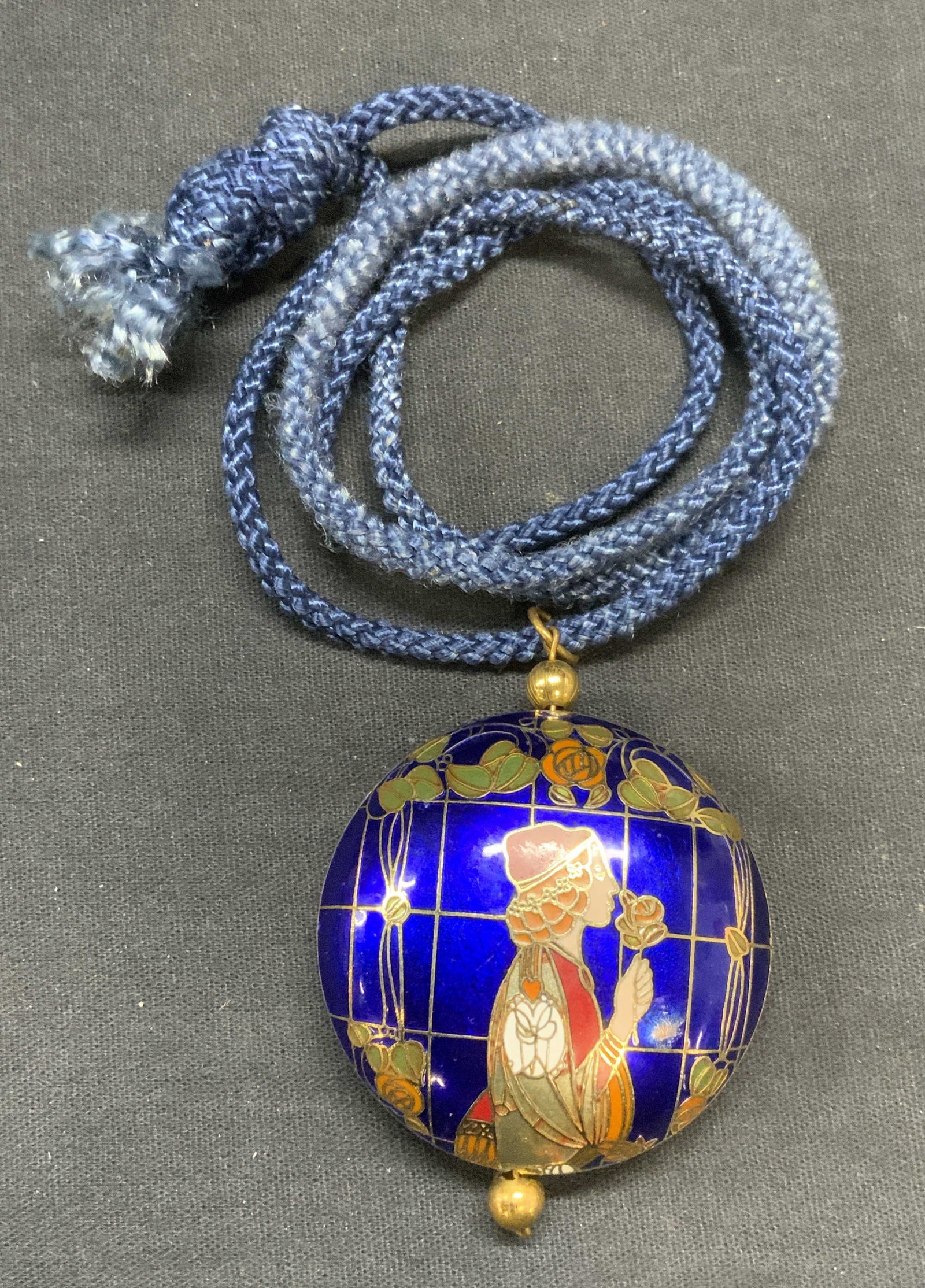 Vintage Figural Cloisonne Pendant Necklace: Vintage blue pendant necklace with gilt cloisonne pendant with figural motif on blue cord. Drop length approx. 13.5 inches. Pendant measures approx. 2 inches diameter. Some surface wear including scra