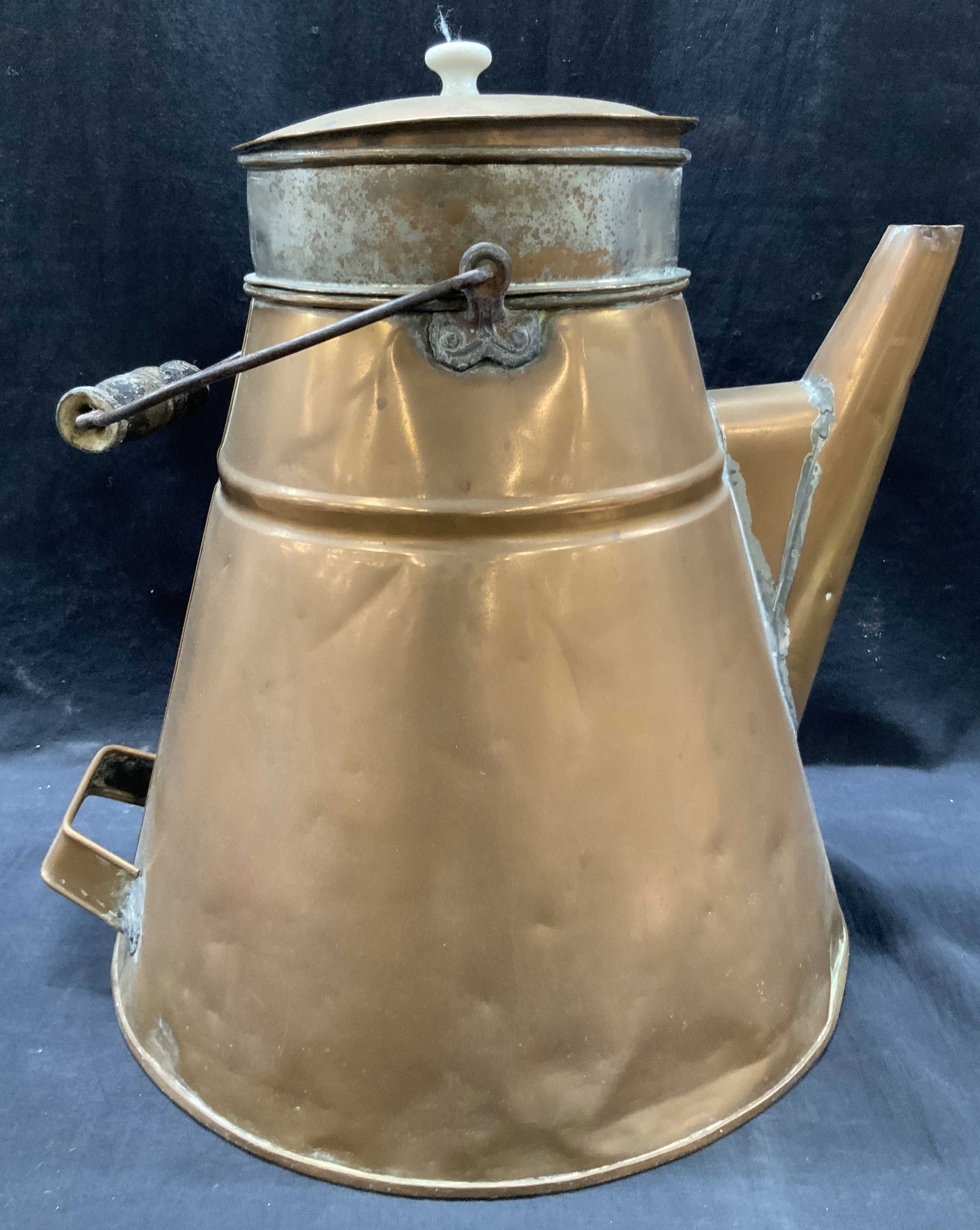 16 Inch Copper Lidded Watering Can: 16 inch tall copper made lidded watering can with iron and wooden top handle and side handle near base. Approx 15 inches long with a 13 inch wide base Evident discoloration and wearing to metal due to