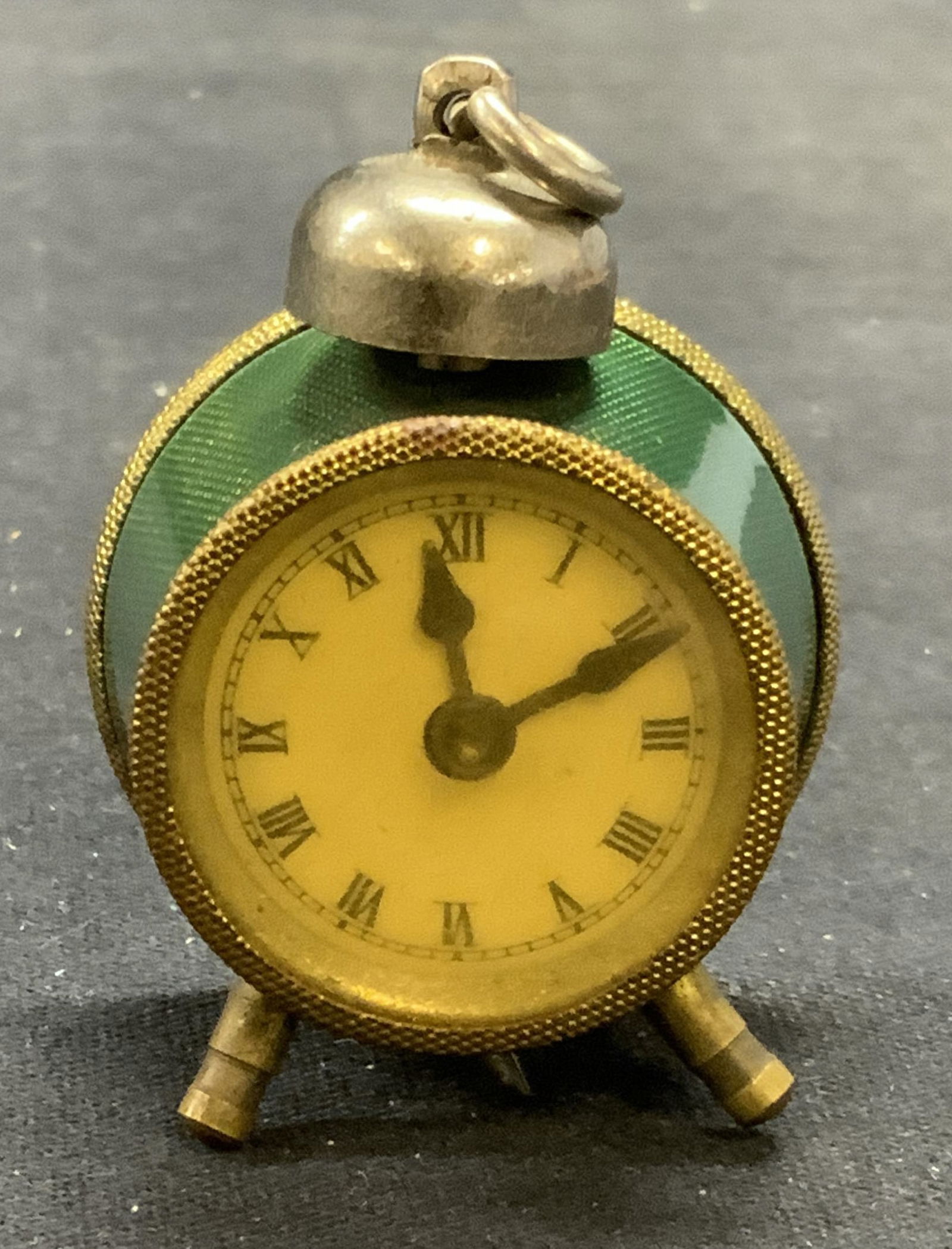 Vintage Gold Tone & Green Alarm Clock Pendant: Vintage gold tone and green detail alarm clock. Two feet to base. Textured surface on metal. Miniature sized. Measures approx. 1.75 x 2 inches. Some surface wear including scratching observed. Unknown