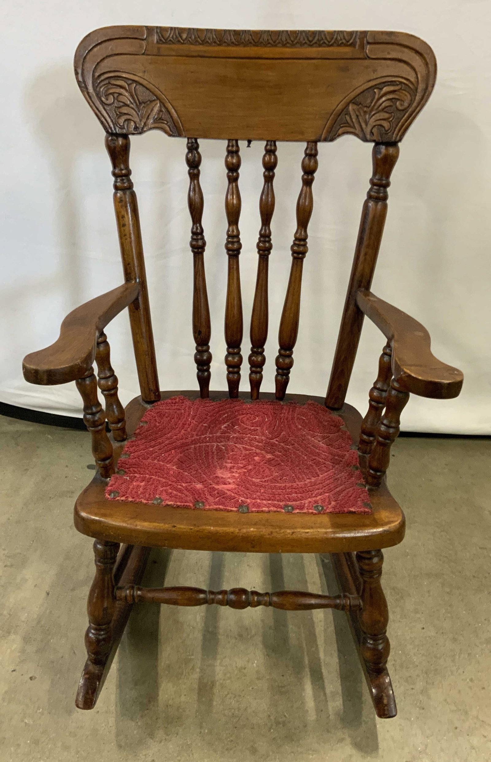 Vintage Carved Wood Childs Rocking Chair: A vintage child rocking chair. Carved wood with a red hued upholstery seat. Nailhead details. Measures approx. 26H x 15.75W x 21.25D in. Surface wear consistent with age, use, and exposure. Losses to 