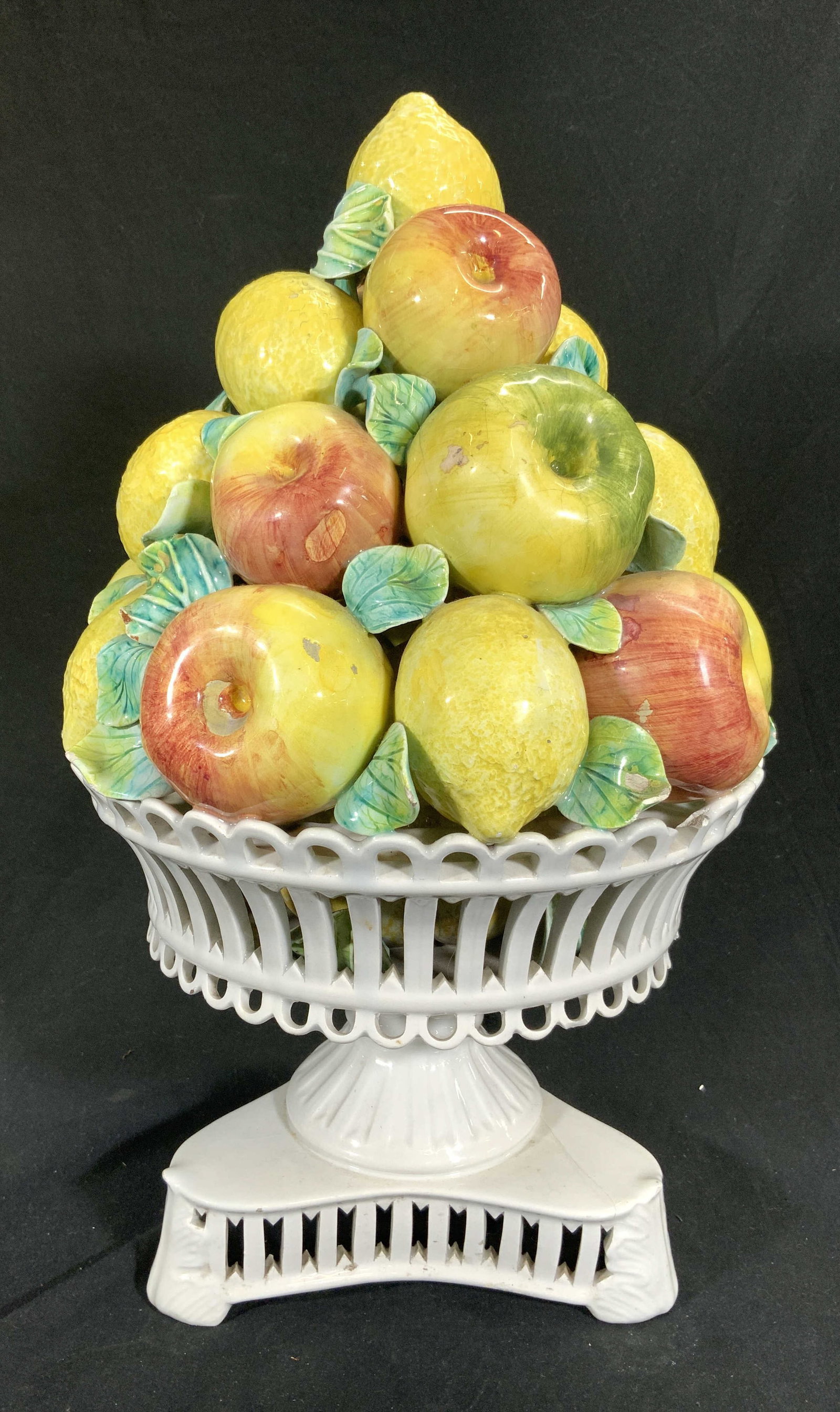 Vintage Porcelain Fruit Arrangement Centerpiece: Piece is vintage and porcelain. White pedestaled base with multi toned fruits (apple & lemons) and leaves arranged and stacked. White toned base has pierced detail. Piece measures approximately 18 inc