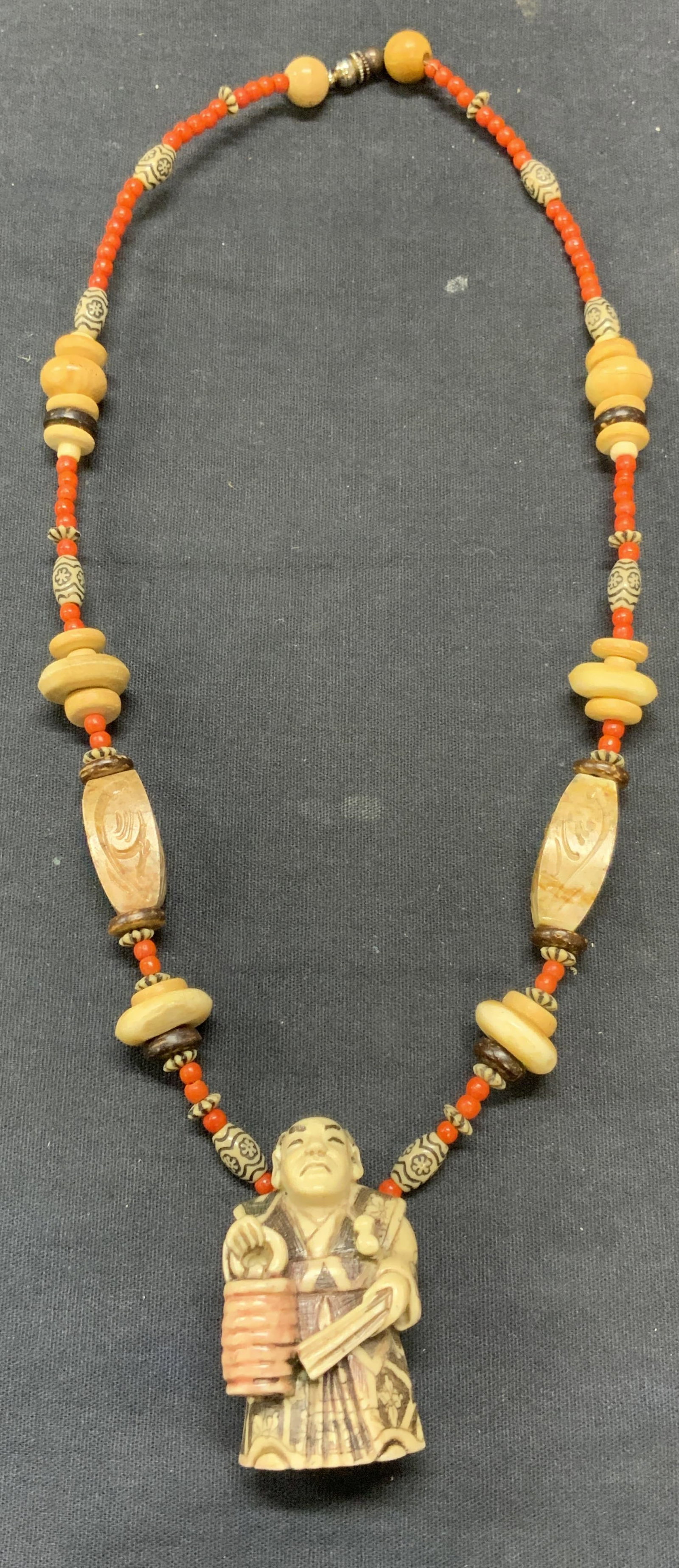 Signed Asian Carved Bone Pendant Necklace: Signed Asian pendant necklace with carved bone beads and figural pendant. Coral seed bead accents. Signed to underside of pendant. Drop length approx. 9.5 inches. Pendant measures approx. 2 x 1 inches