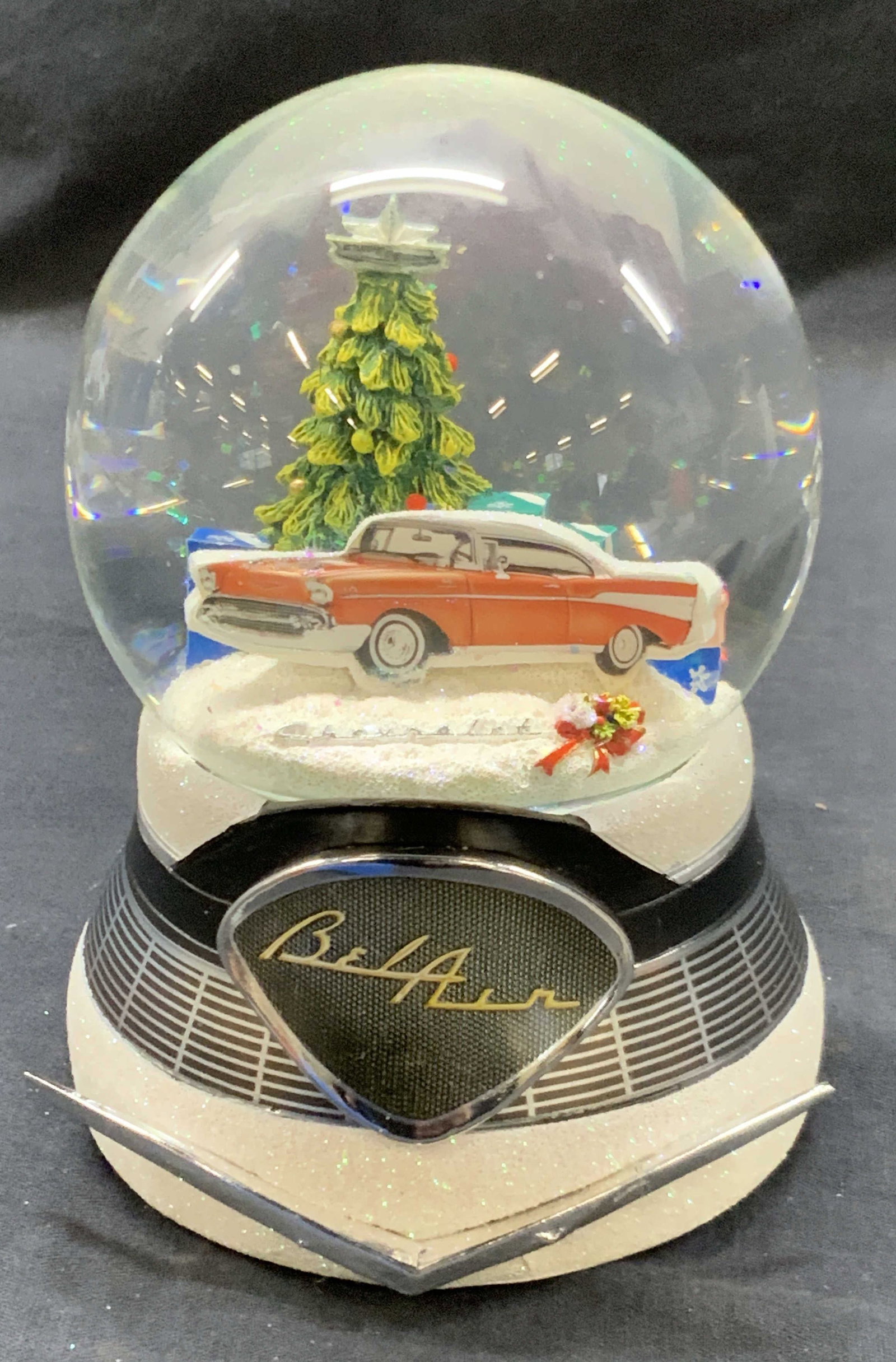 Bel Air Car Glitter Globe: A glitter globe marked Bel air on front with the interior of the globe having a Christmas tree with presents and a red bel air car with the bottom half of the globe resembling a car grill. Marked on u