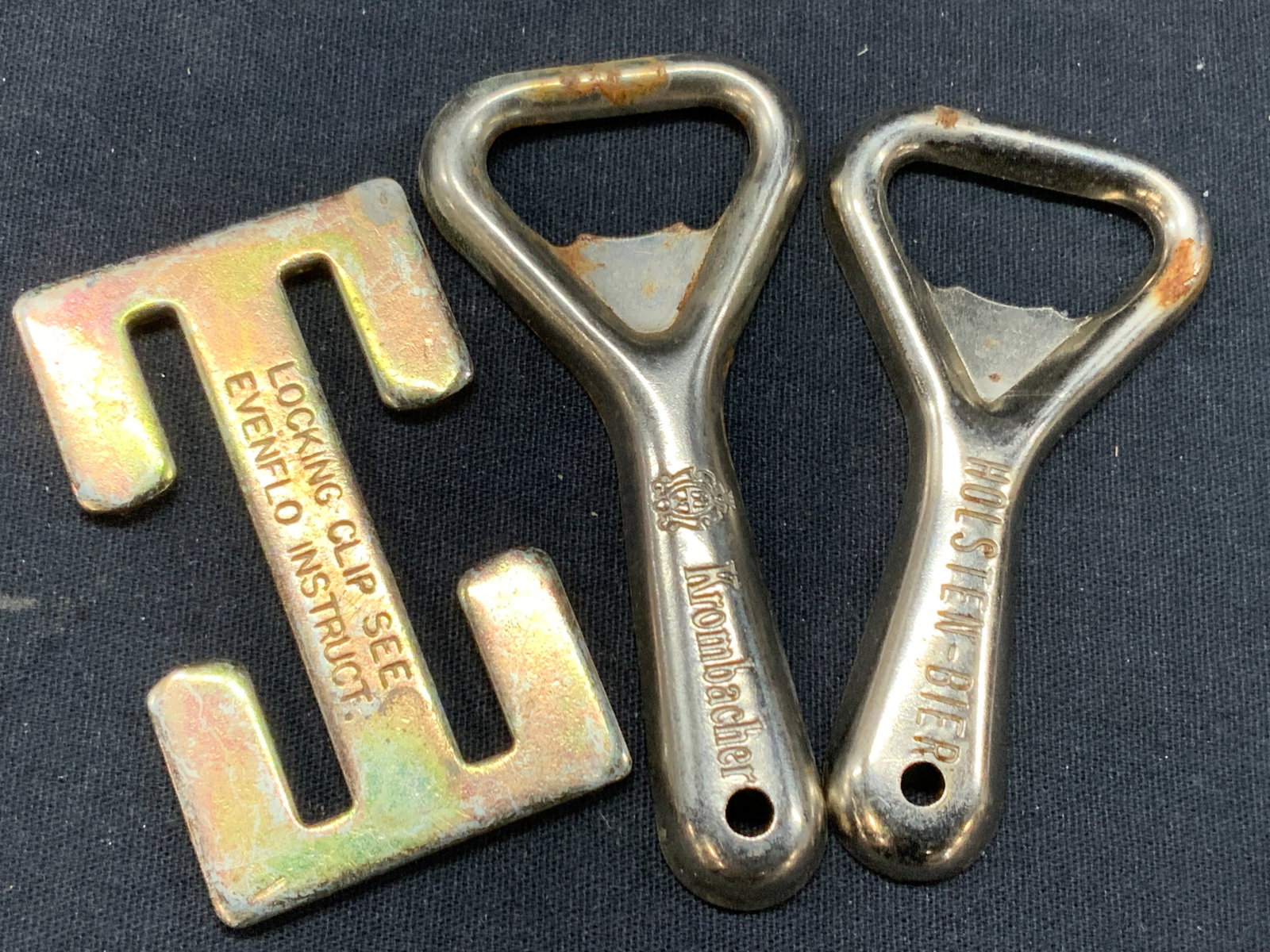 Lot 3 Vtg Metal Bottle Openers + Germany: Lot of 3 metal accessories. 2 German marked metal bottle openers, marked Holstein-Bier and Krombacher. Approx 3 inches long and 1 metal lock clip. Approx 1.25 x 1.25 inches Moderate wearing to metal. 