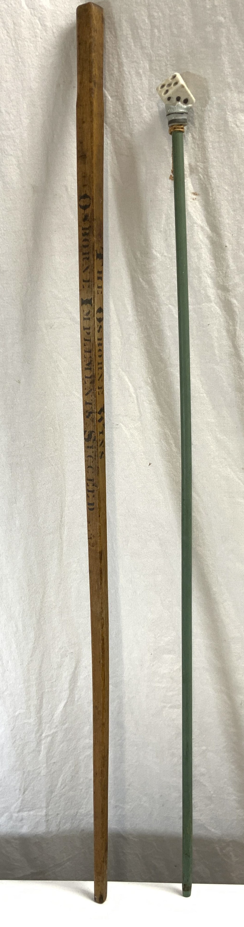 Lot 2 Vntg Wood & Porcelain Walking Sticks: Lot includes 1 tan toned wooden walking stick marked THE OSBORNE WINS OSBORNE IMPLEMENTS SUCCEED and 1 green toned wooden walking stick with die form porcelain top. Largest piece in lot measures appro