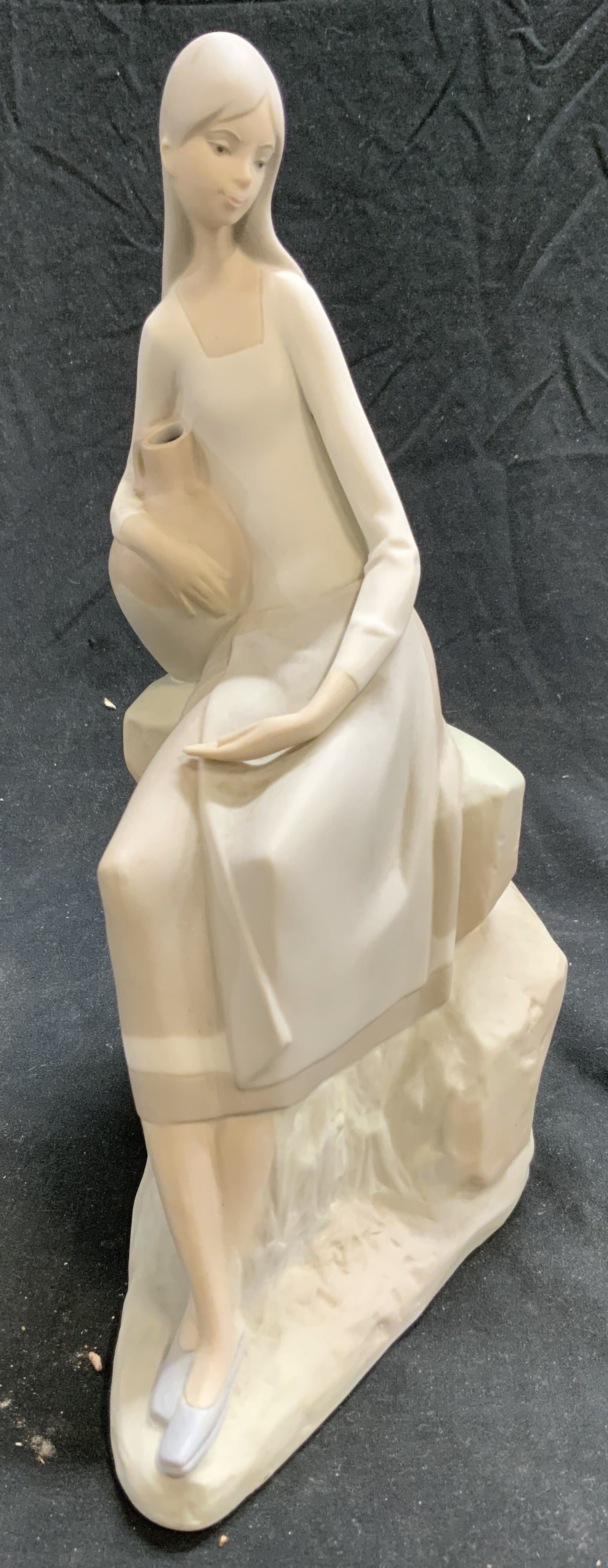 NAO LLADRO Porc Girl On Rocks With Water Spain: Underside is inscribed NAO MADE IN SPAIN. Piece depicts a female figure sitting on rocks with a jug of water. Piece is vintage and porcelain. Measures approximately 10 inches tall 7 inches deep 4 inch