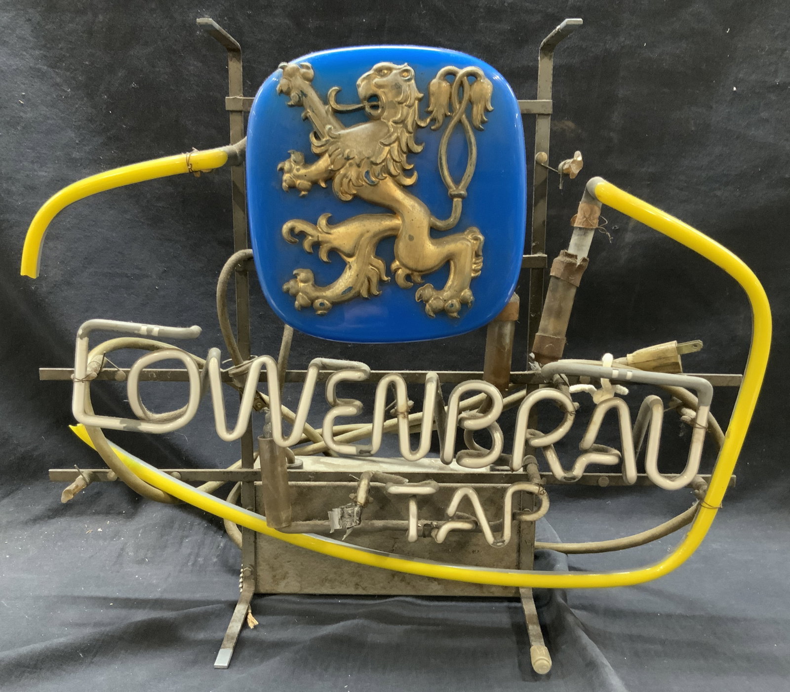 Vtg Lowenbrau Tap Neon Sign: Vintage neon sign marked Lowenbrau tap, depicting a lion in the center of a blue light with a yellow ring light around the body. Approx 16 inches tall and 21 inches wide. Evident wearing and yellow se