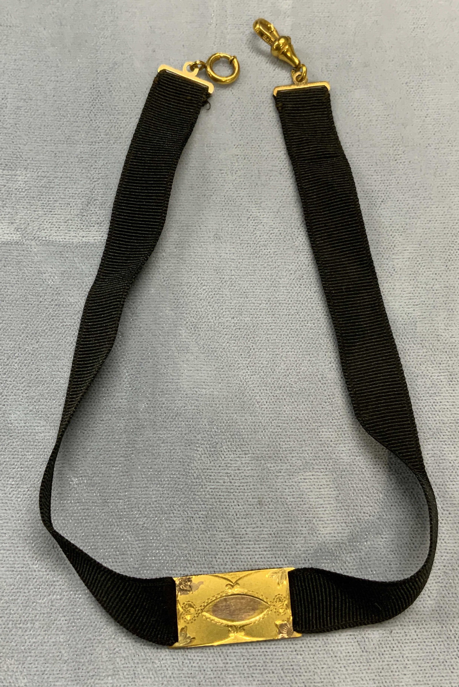 Gold Tone Black Ribbon Choker Necklace: Black ribbon choker necklace with gold tone accent. Embossed scroll motif. Measures approx. 11.5 inches long. Some surface wear including scratching observed. Estate jewelry, costume jewelry, cocktail