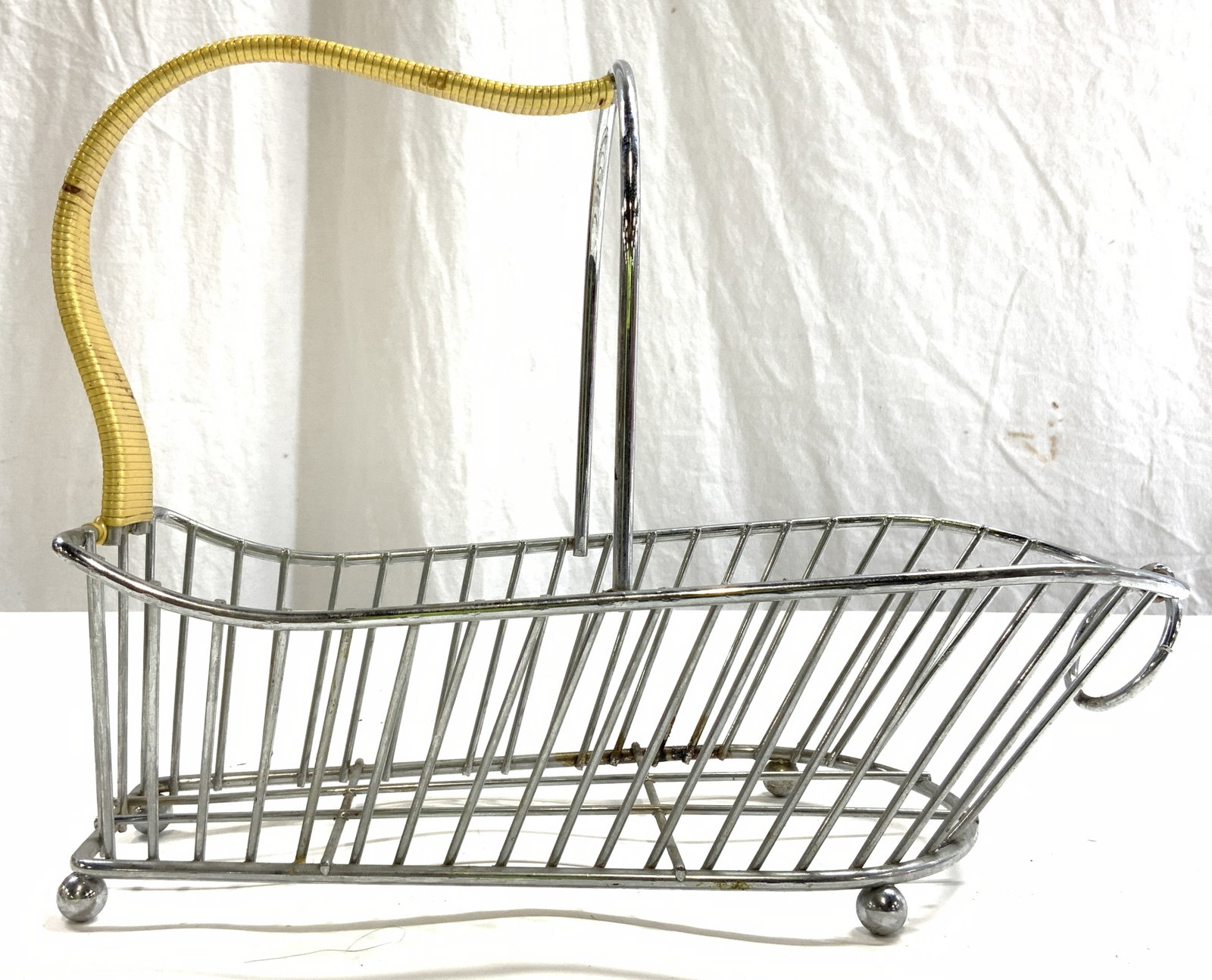 Footed Metal Wine Bottle Serving Basket: Basket is silver toned and metal. Piece has tan toned wrapping around handle. Basket has 4 spherical shaped feet. Piece measures approximately 12.5 inches long 9 inches tall 5.5 inches wide. Basket, w