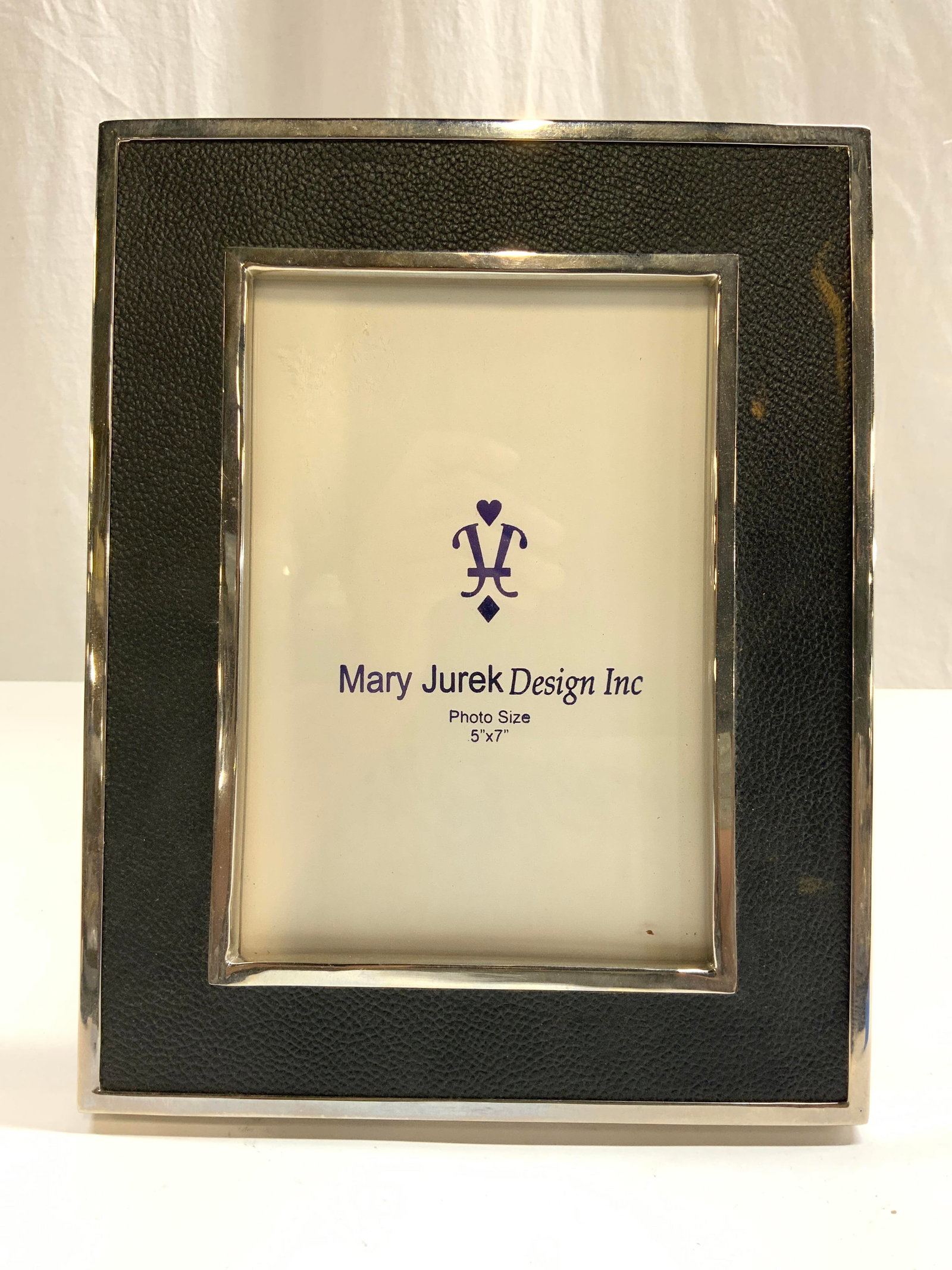 MARY JUREK DESIGN Pebbled Leather & Metal Frame: Frame trademarked MARY JUREK DESIGN INC. Piece is black toned pebbled leather and silver toned metal. Frame has support on back for piece to stand on its own. Silver toned plaque on backside reads MJ.