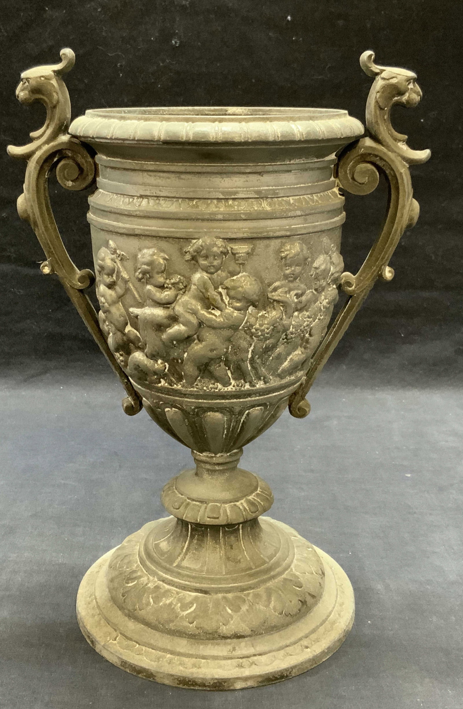 Vtg Silver Tn Cherub Motif Footed Urn Vase: Vintage silver tone metal footed urn vase with raised cherub motif and scroll pattern. Piece has weight. Measures approx. 7 x 5.25 x 9 inches. Surface wear including scratching and patina observed. Ur