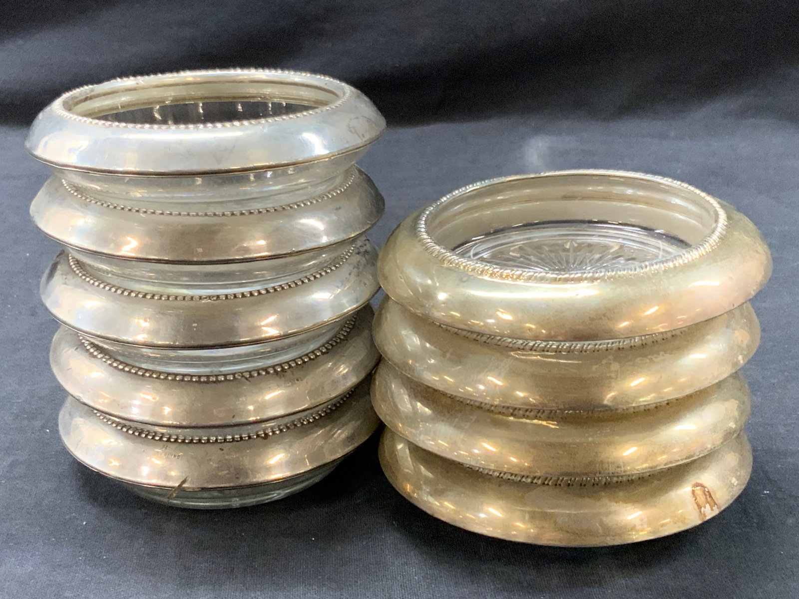 9 Sterling Silver Overlay Glass Coasters: Lot of 9 sterling silver overlay glass coasters. 4 at 4.25 inch diameter and 5 at 4 inch diameter. Each stamped sterling on overlays. Moderate wearing to sterling with denting and scratches to glass.