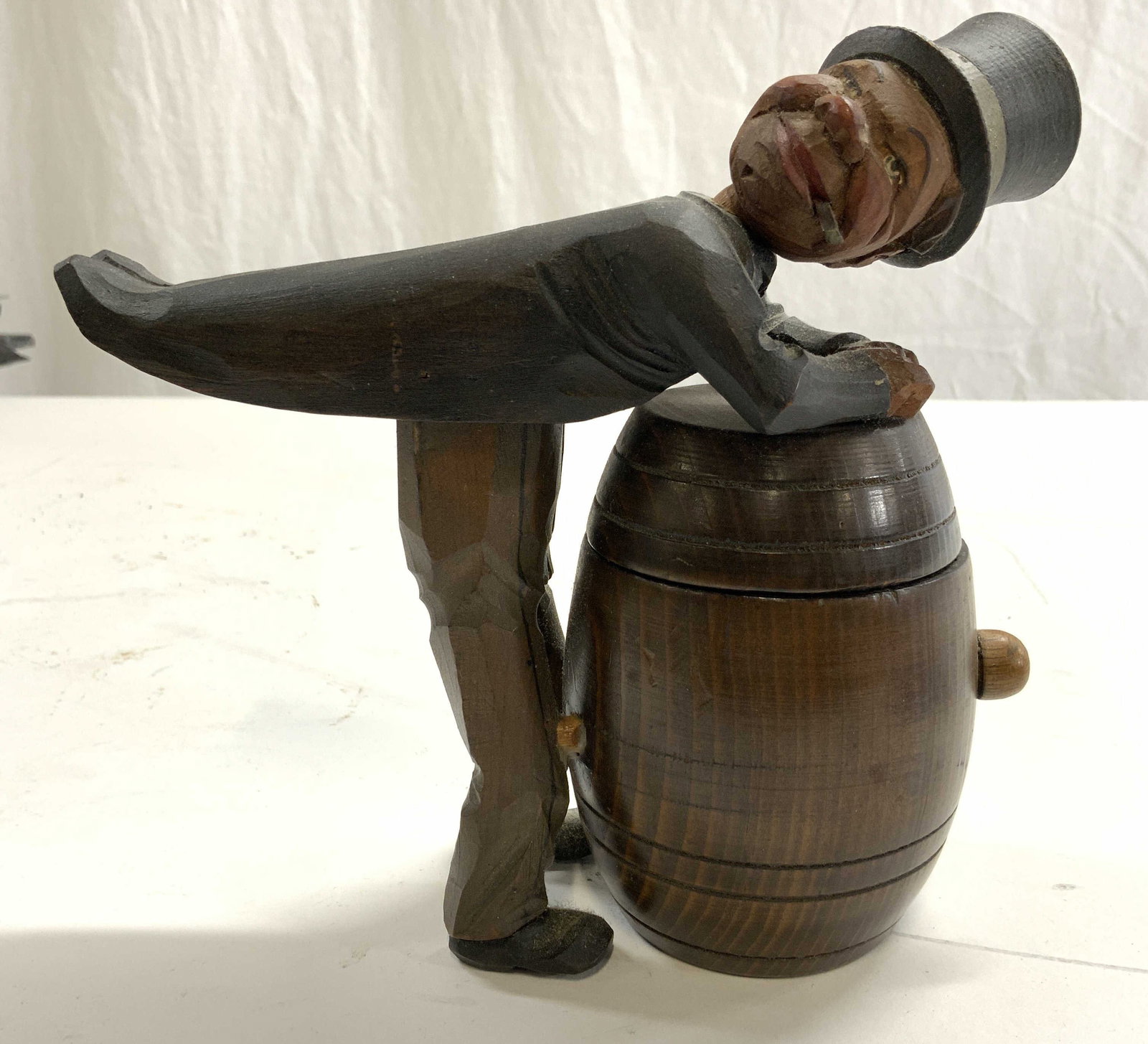 ANRI Vntg Wood Man Over Barrel Cigarette Holder: Piece appears to be ANRI no apparent markings. Sculpture depicts a male figure in a suit bent over a wooden barrel. Lid opens when pressing down on coat tails. Measures approx 6.5 inches tall & deep 2