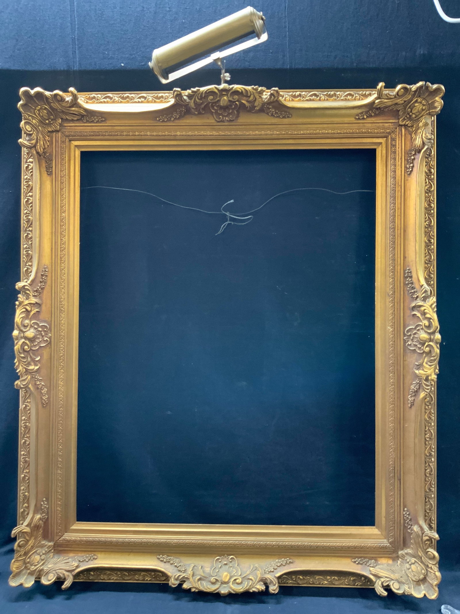 Gilt Ornate Carved Wooden French Style Frame: Ornately crafted wooden carved and plaster made frame with raised French style scroll motifs with floral detailing and scrolled on back paneling. Comes with brass light piece on top, with no cord. Ado