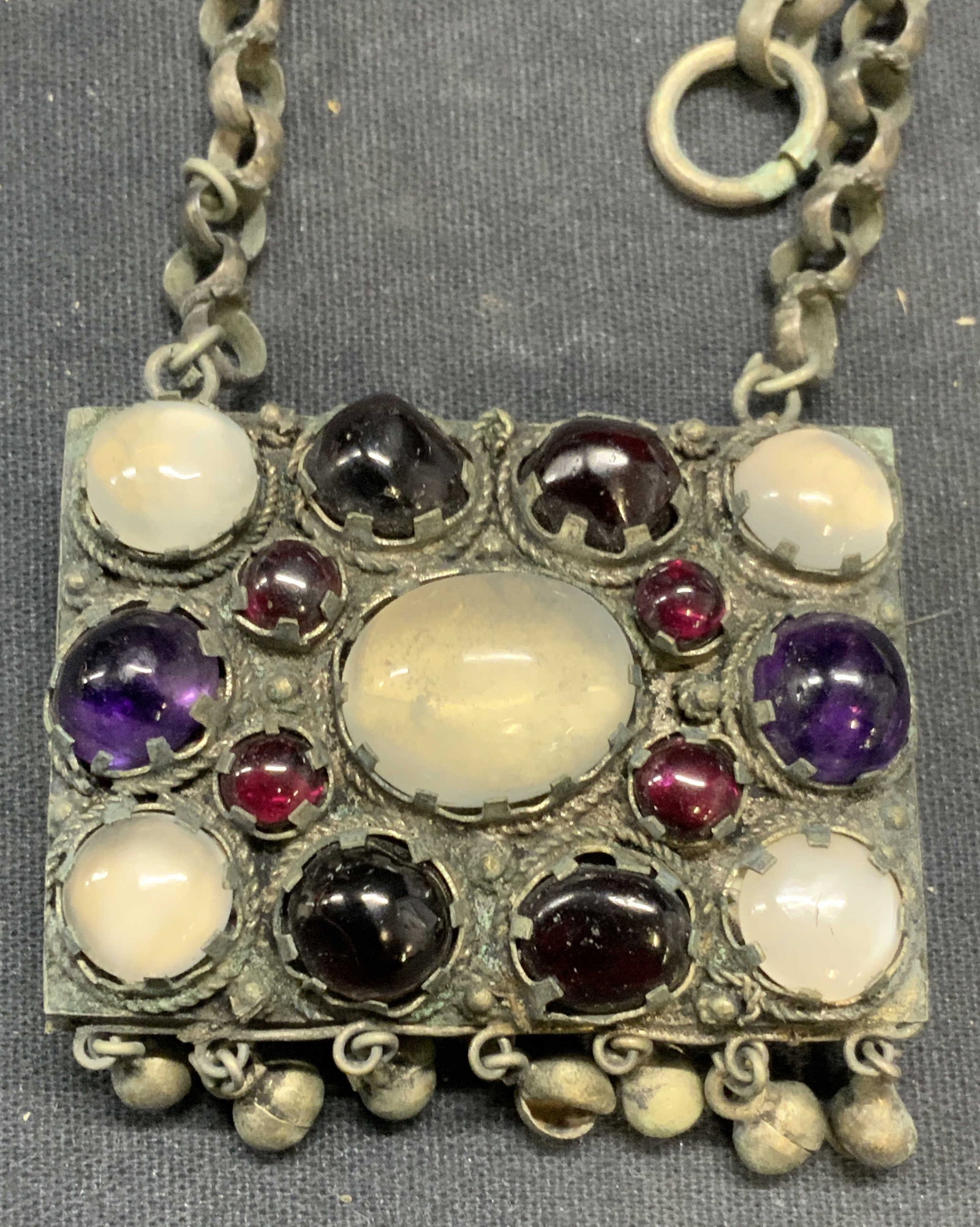 Vintage Silver Tone Amethyst & Garnet Necklace: Vintage silver tone pendant necklace with polished amethyst, garnet, and glass decoration. Embossed floral motif pendant. Drop length approx. 13 inches. Some surface wear including scratching observed