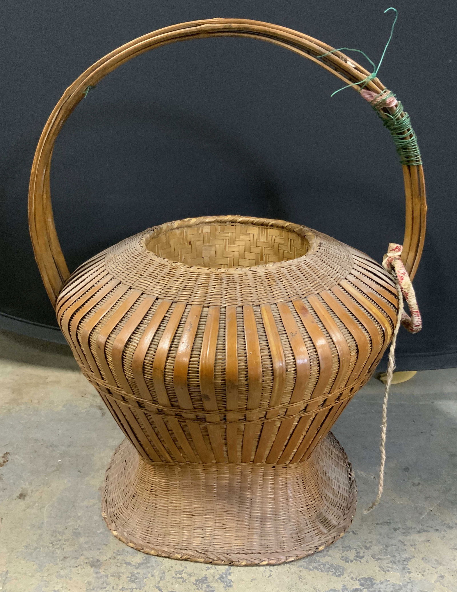 Vintage Woven Top Handle Basket 18.5in: A vintage woven basket with a top handle. Brown hues. Measures approx. 18.5H x 15W in. Some fabric material and wire material attached to basket. Some surface wear consistent with age, use, and exposu