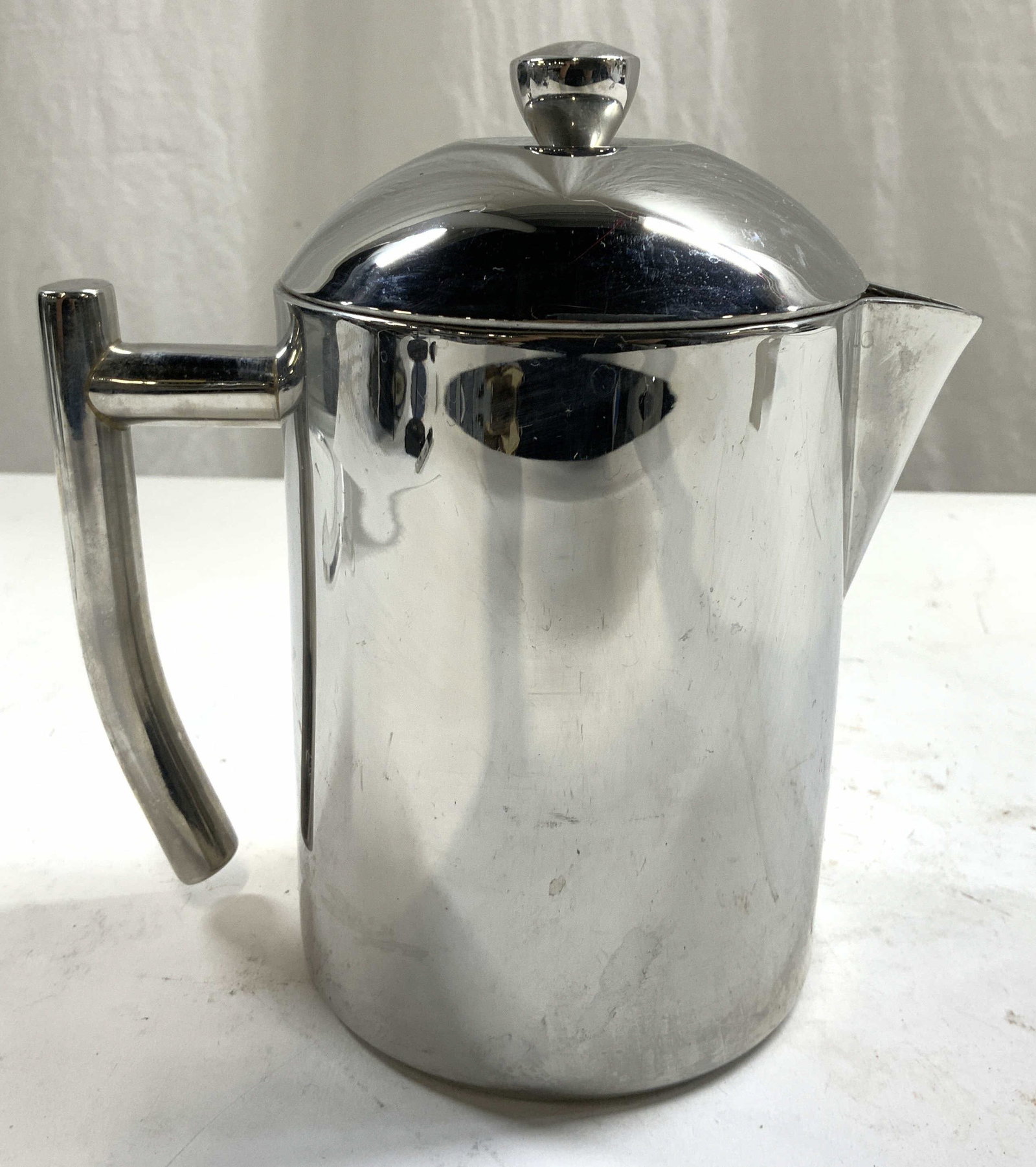 FRIELING Metal Coffee Pot W Lid: Underside is marked FRIELING. Coffee pot is silver toned and metal. Piece has lid with knob style handle. Coffee pot has uniquely shaped handle. Piece measures approximately 7 inches tall 6.75 inches 