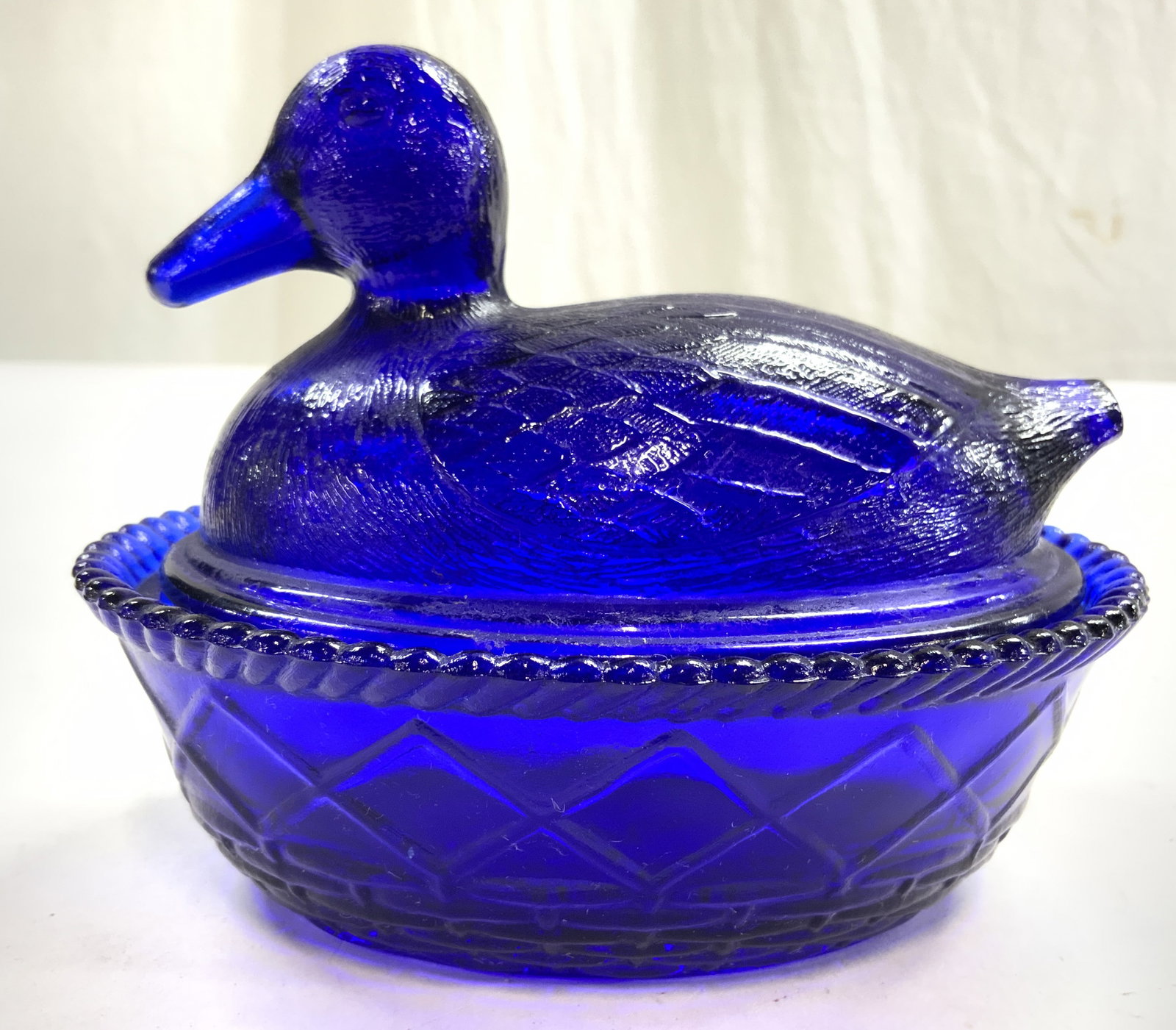 Cobalt Glass Vessel W Duck Lid: Vessel is cobalt blue toned. Piece has basket form vessel & duck form lid. Piece has textural detail. Rim has rounded teeth. Piece measures approximately 5.5 inches wide 4.25 inches deep & tall. Vesse