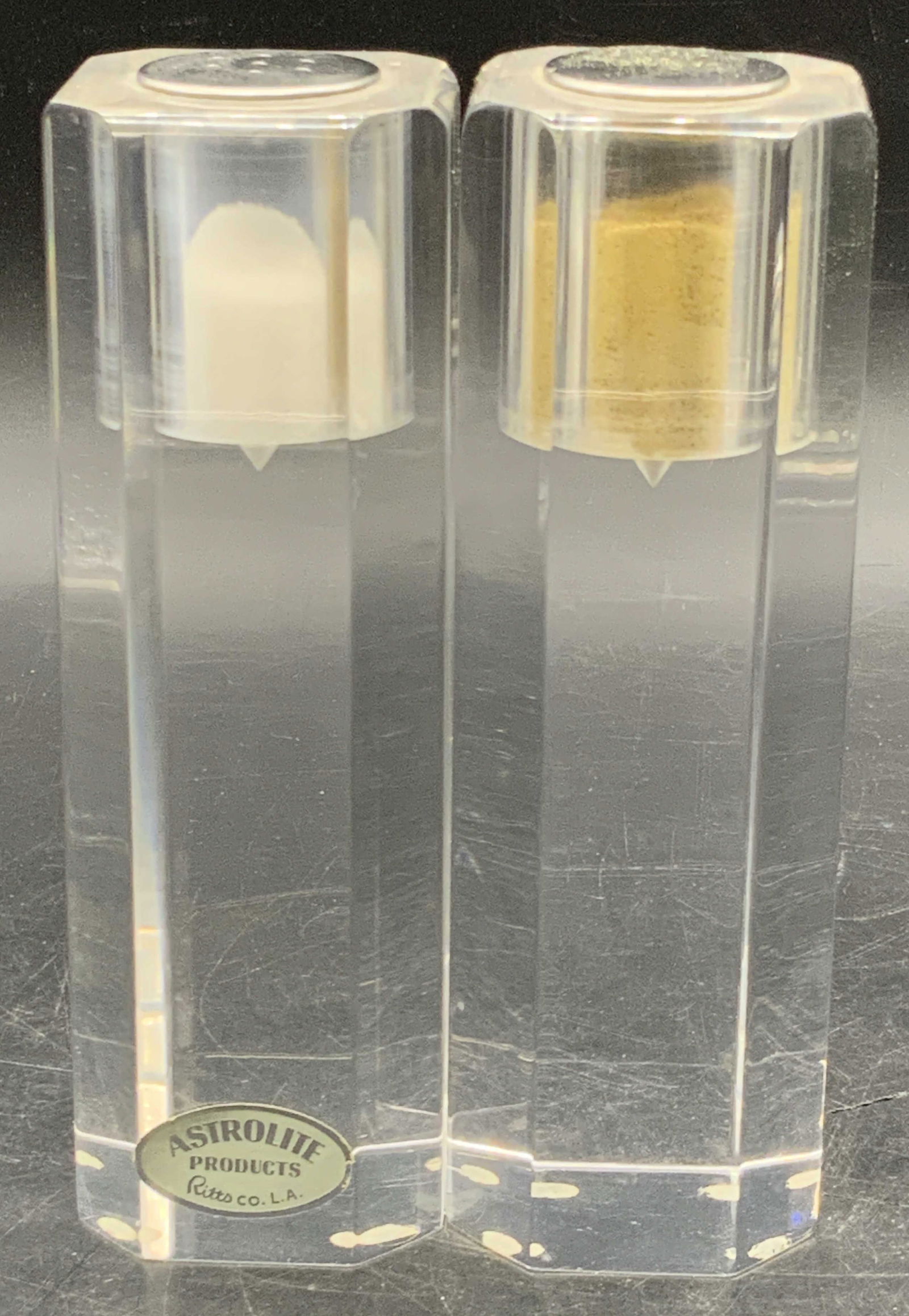 Pr ASTROLITE Ritts MCM Faceted Lucite Shakers, USA: A pair of vintage mid century modern cylindrical faceted clear lucite salt & pepper shakers. Pierced metal tops for dispensing seasoning. Sticker to obverse of one shaker reads ASTROLITE PRODUCTS, RIT