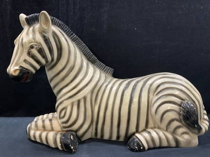 24 In Long Plaster Zebra Sculpture: Approx 24 inches long and 17 inches tall. Plaster crafted zebra sculpture of a seated zebra with painted black stripes and accents throughout Evident cracking and holes to plaster and cracking to
