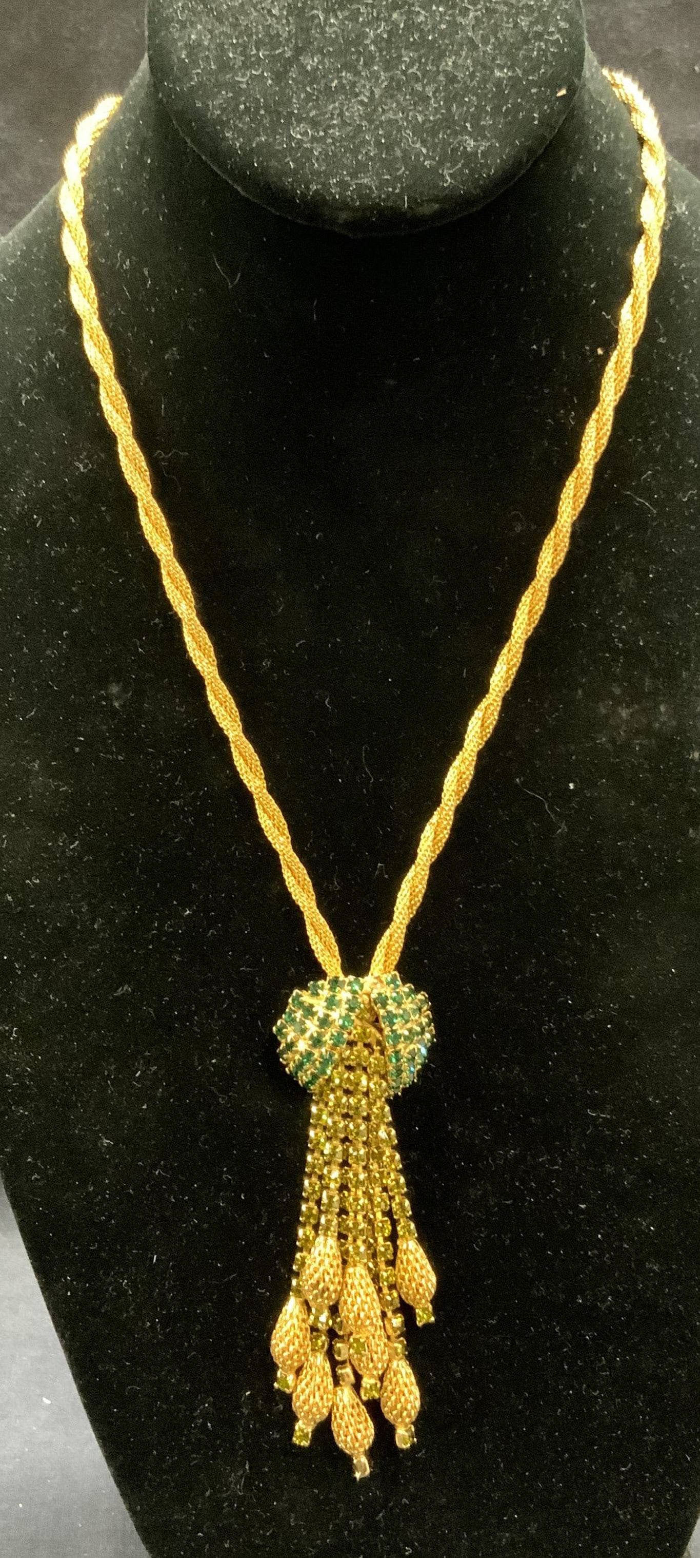 Vintage Gold Tone Green Crystal Necklace: Vintage gold tone twisted chain pendant necklace with green crystal decorated tassel pendant. Drop length approx. 9.5 inches. Pendant and tassel measure approx. 3.5 inches long. Includes jewelry pouch
