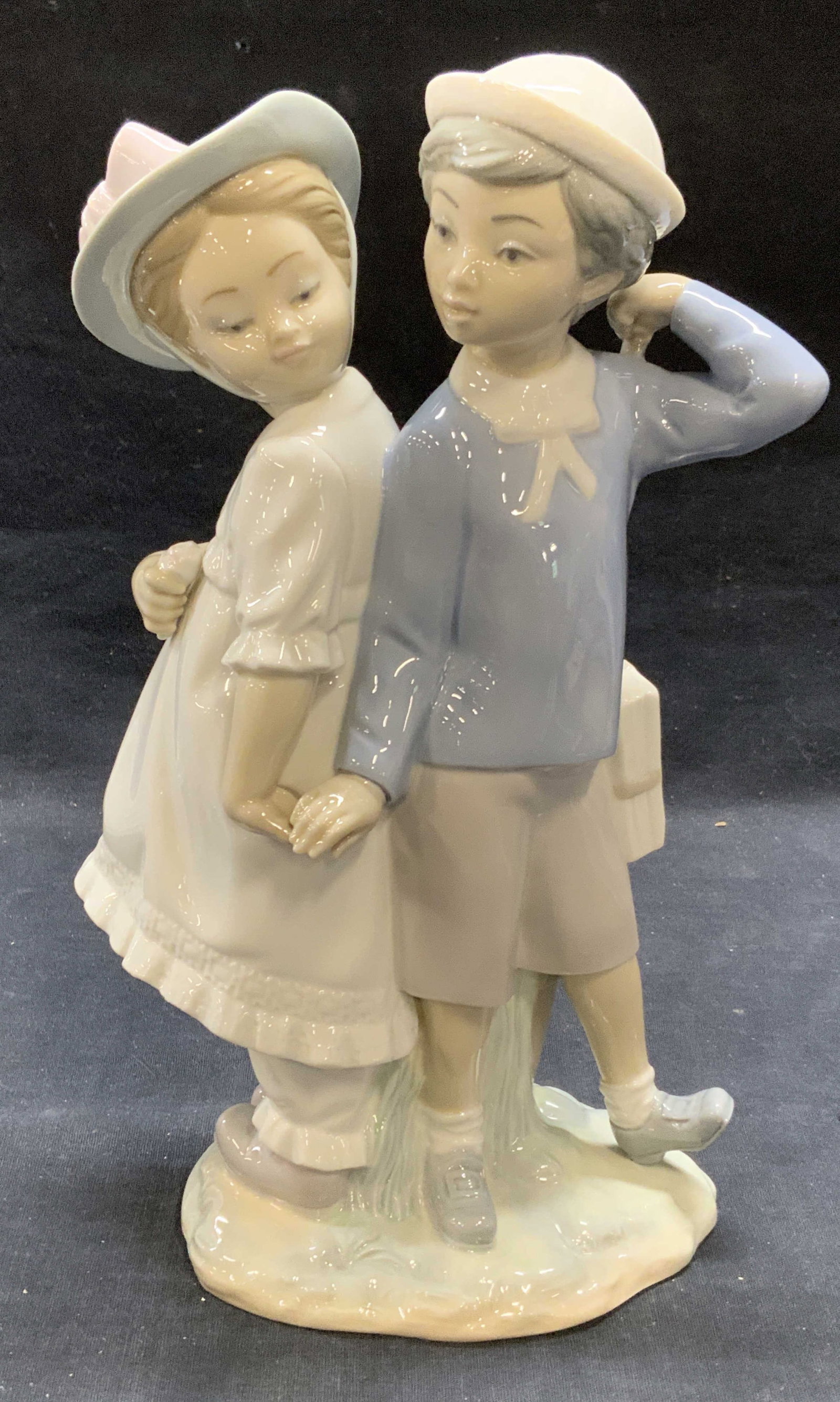 Lladro Porcelain Children Figurals, Spain: Lladro porcelain figurine. Boy and girl in hues of pink and blue. Signed to underside. Measures approx. 6.5 x 3.5 x 10 inches. Some surface wear including scratching observed. Lladro, Lladro figurine,