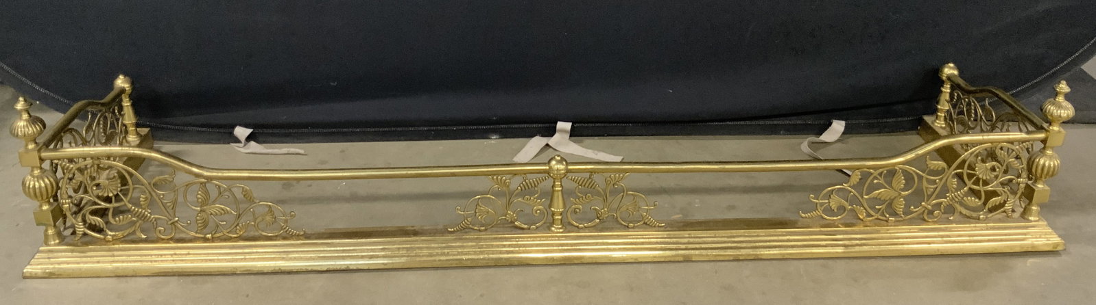 Vintage Brass Fireplace Fender: A vintage polished brass fireplace fender. Scrolled foliage motifs. Measures approx. 10H x 16D x 57.75W in. Patina present. Some surface wear consistent with age, use, and exposure. Denting present. S