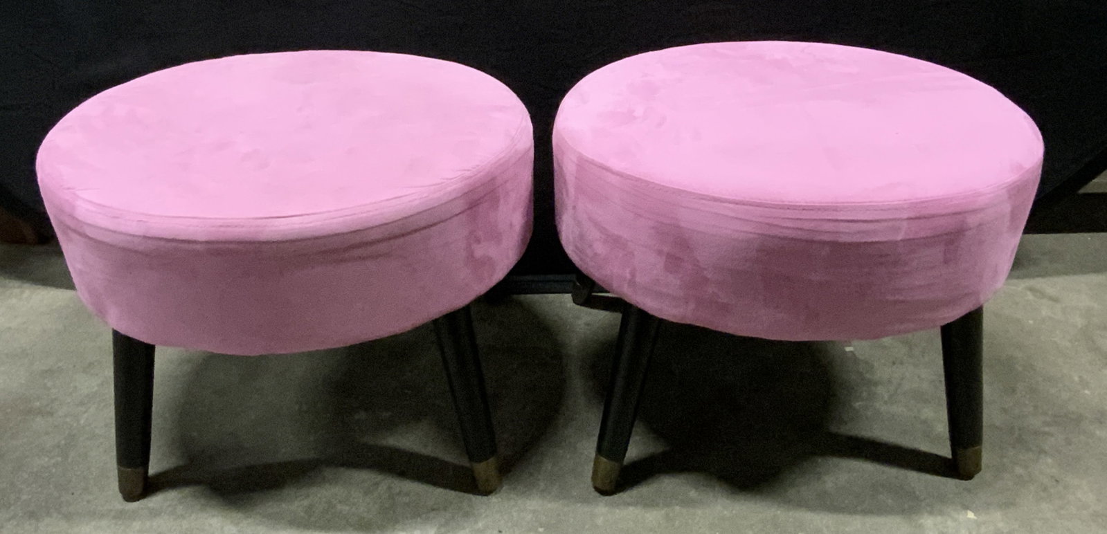Pair Pink Upholstery Oval Form Ottomans / Stools: A pair of soft hand pink hued upholstery ottomans / stools with black splayed legs. Zippered underside. Measures approx. 16H x 21W x 17.75D in. Legs need tightening / adjustment. Losses to hardware. S