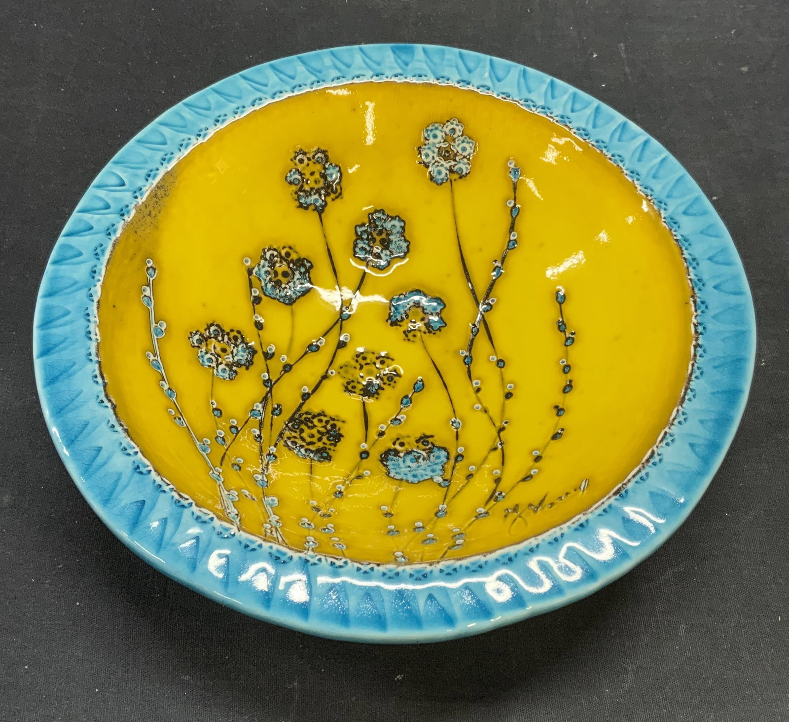 By Nunes Signed Floral Ceramic Bowl: Stamped By Nunes bowl with hand painted floral motif in yellow and blue. Signed illegibly to front and underside. Measures approx. 9.25 x 2 inches. Some surface wear including scratching observed. By 