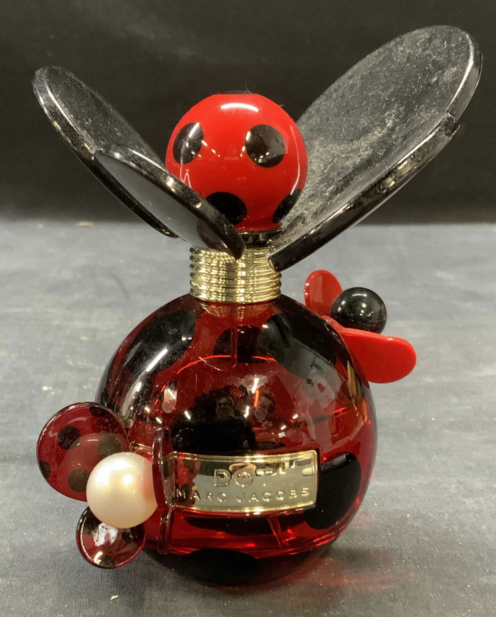 Marc Jacobs Dot Eau de Parfum: Marc Jacobs Dot eau de parfum. 3.4 fl oz size, partially filled. Red and black glass bottle with acrylic top and faux pearl decoration. Measures approx. 5 inches tall including top. Some surface wear