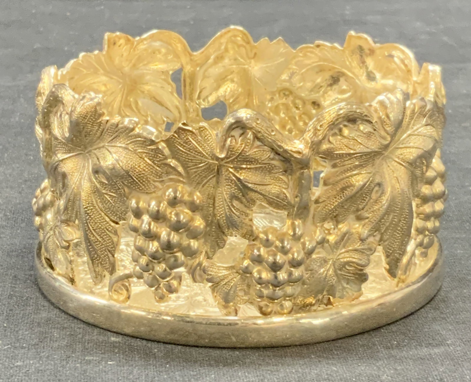 Topazio Silver Plated Wine Bottle Coaster: Topazio silver plated wine bottle coaster. Pierced raised grape vine motif. Trademarked to underside. Made in Portugal. Measures approx. 4 x 2 inches. Some surface wear including scratching and loss t