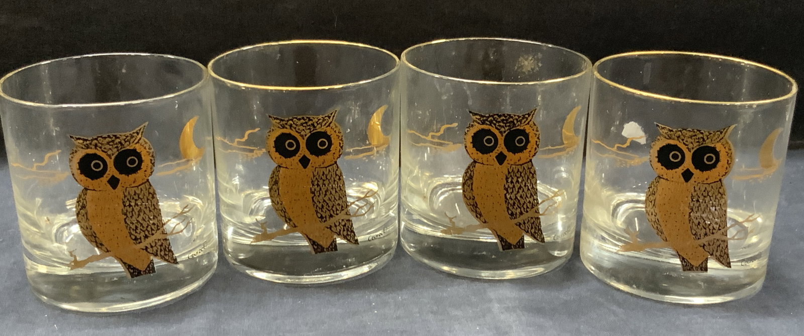 Set 5 Couroc Gilt Owl Barware Glasses: Set of 5 bar glasses with gilt edges and gilt owls on sides. Marked on glasses Couroc. Approx 3.24 inches tall and 3 inch diameter. Evident cracking to some glasses and overall wearing to gilt. Gilt g