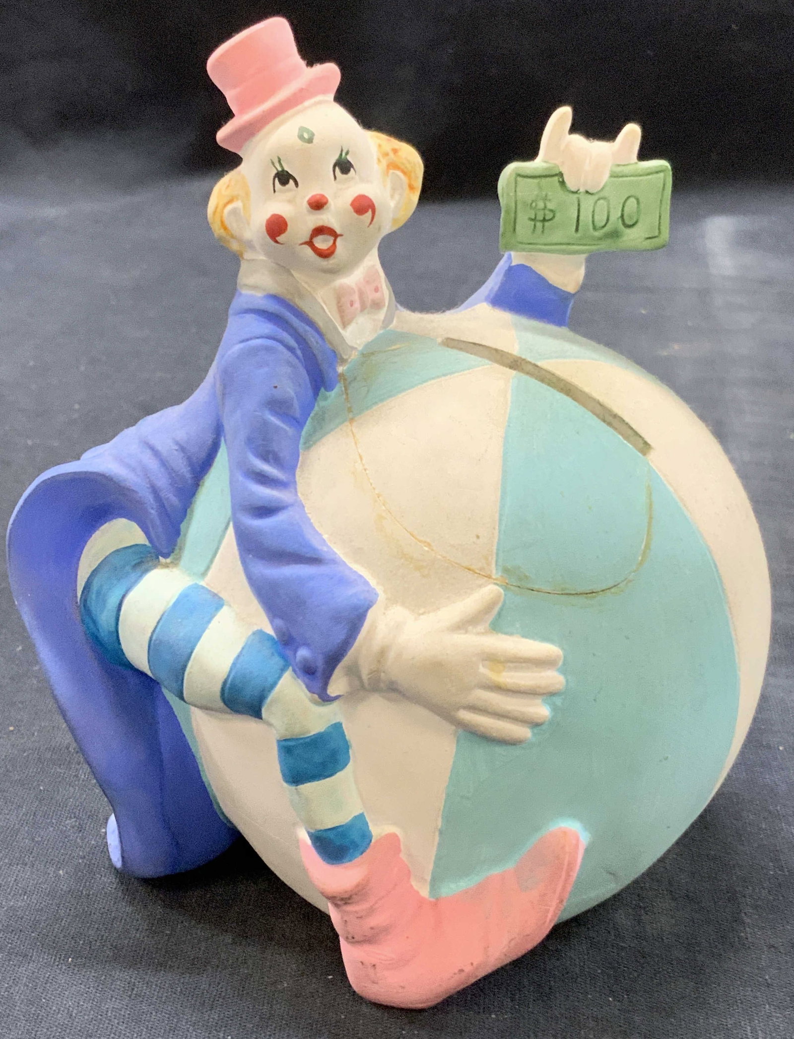 Vtg Ceramic Clown Coin Bank: Vintage ceramic coin bank with a clown hugging a large ball with a hundred dollar pill in his hand. Approx 6 inches tall. Moderate wearing to ceramic and evident repairing to ball on side. Ceramic dec