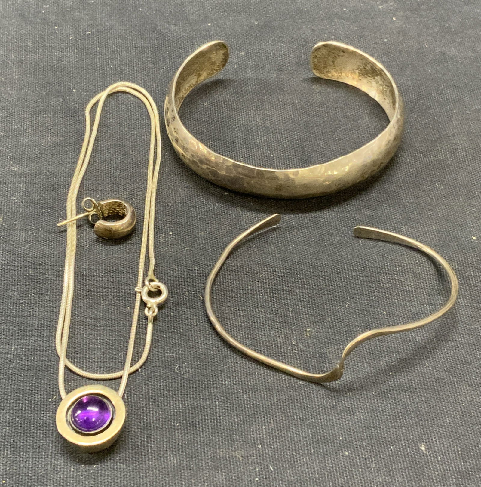 Lot 4 Sterling Silver Bracelets & Necklace: Sterling silver pendant necklace with amethyst gemstone. Drop length approx. 8 inches. 2 sterling silver cuff bracelets. Larger measures approx. 2.25 inches wide. Sterling silver hoop earring. Single