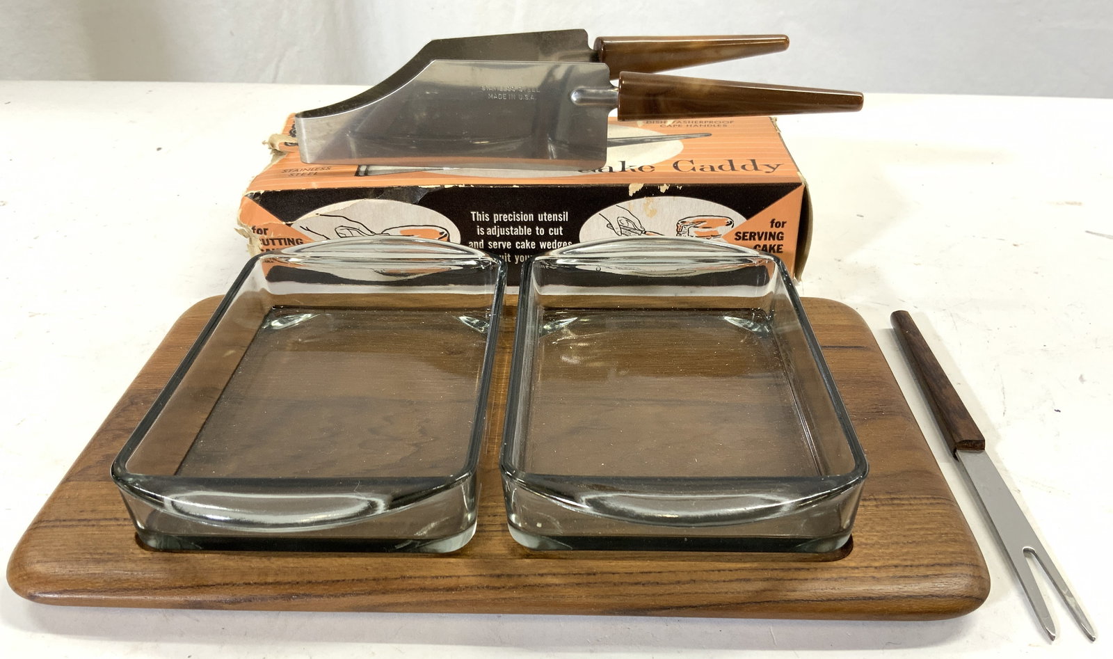 Lot 5 Kitchen Serveware Accessories USA+: Lot includes 1 wooden serving tray 2 glass serving dishes, 1 hors D oeuvres fork with wooden handle & 1 Cake caddy with original box (inscribed MADE IN USA). Wooden serving tray measures approximately