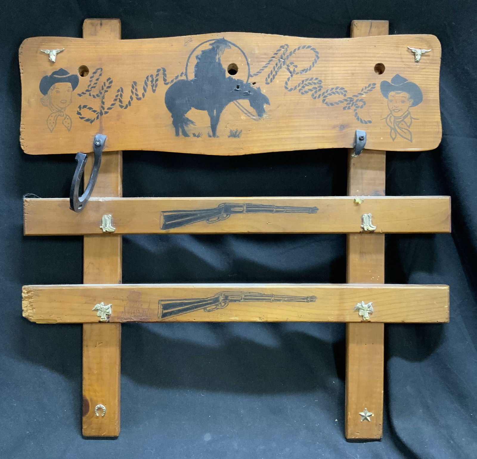 CHILDS WESTERN WOODEN TOY GUN RACK: Toy gun rack is light brown toned & wooden. Piece has depiction of male & female figure wearing cowboy hats. Piece has black toned detail depicting a cowboy on a horse, & rifles. Piece has 1 hook & ar