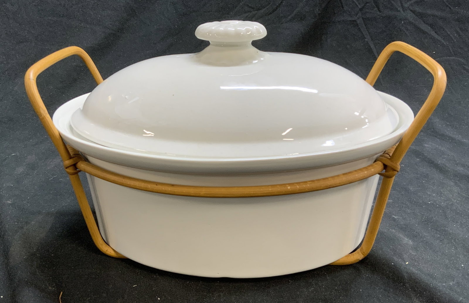 Arabia Casserole Dish in Bamboo Caddy, Finland: White porcelain casserole dish with lid/ serving dish. Oval shape and sits in a bamboo caddy with handles. Marked Arabia Finland. Steam on lid. Measures 10.25 in. Long x 8 in. Wide. 4 in deep ( withou