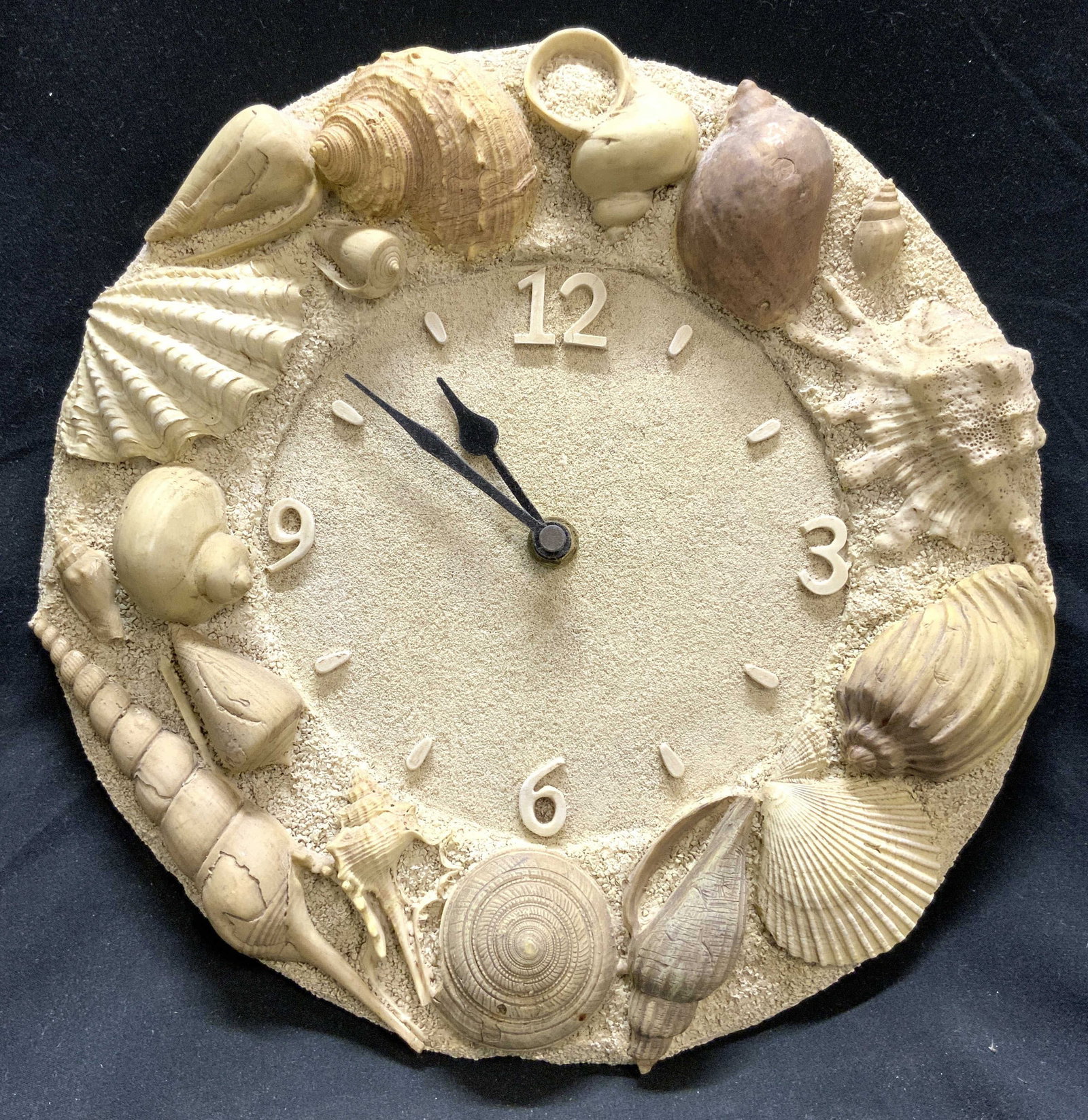 Resinous Seashell Detailed Wall Clock: Wall clock is sand toned. Piece appears. One crafted from a resinous material, possibly Wooden. Clock has raised seashell detail around edges. Piece has black toned hands. Clock measures approximately