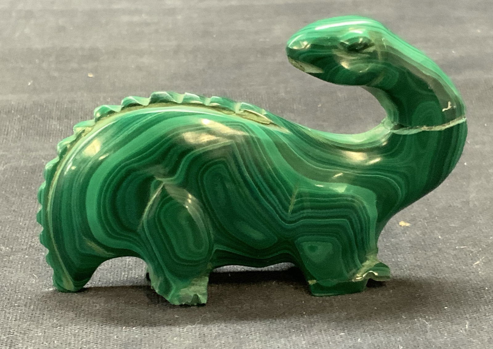 Carved Malachite Dinosaur Figural: Carved malachite stone dinosaur motif Figural. Measures approx. 3 x .75 x 1.75 inches. Surface wear including scratching, chipping, and previous repairs observed. Malachite, malachite figurine, malach