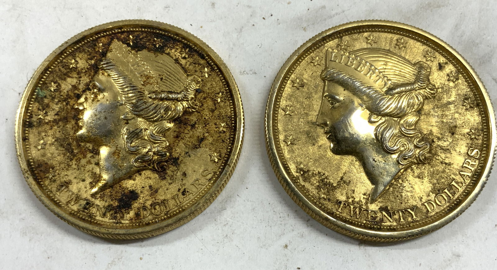 Lot 2 Gilt Metal Coin Coasters: Lot includes 2 coasters. Each have gold toned gilt finishes. Each are circular shaped with coin form. Each measures approximately 3.75 inches diameter. Liberty, twenty dollars, paperweights , collecti