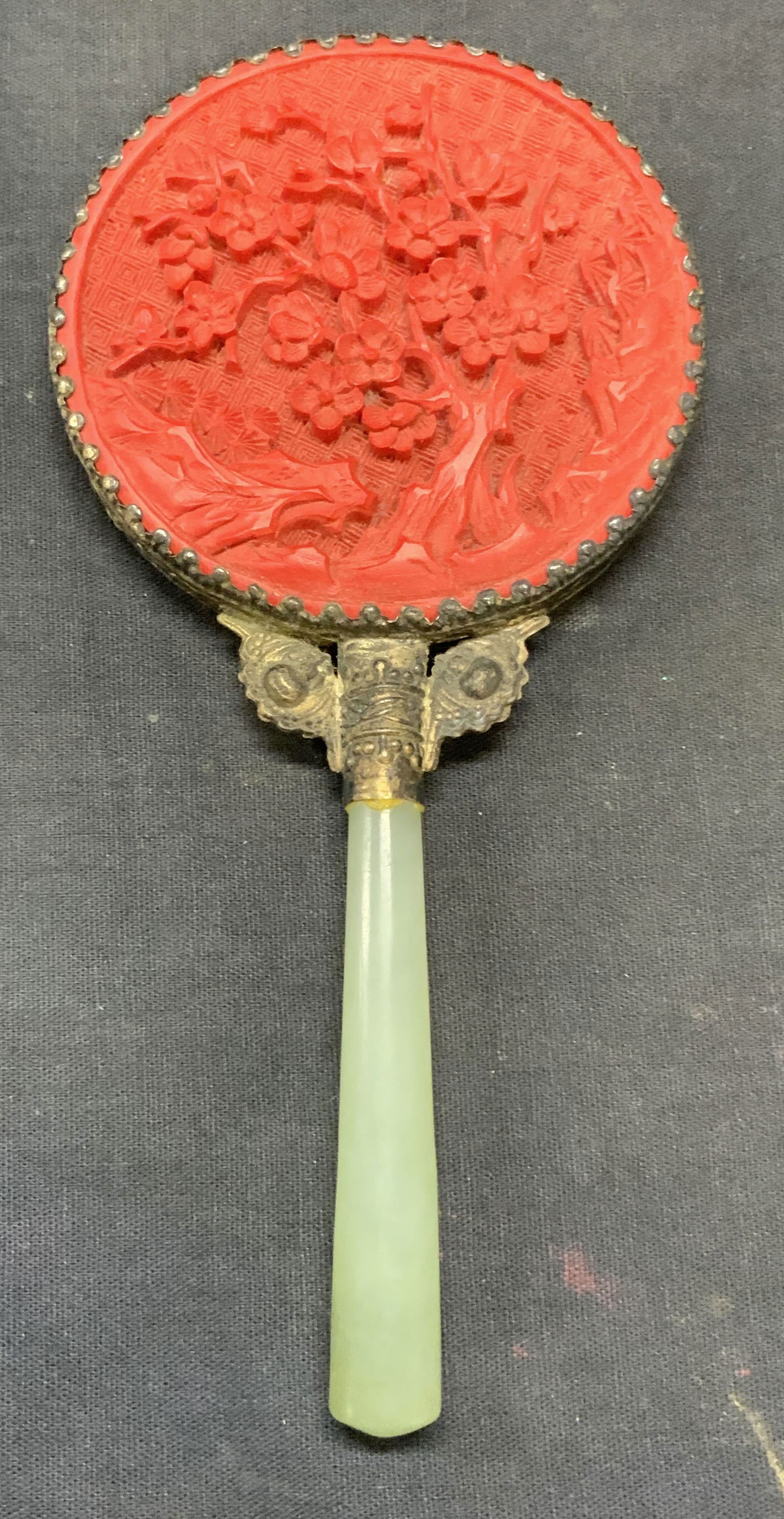 Vintage Cinnabar Style Green Stone Hand Mirror: Vintage carved cinnabar style hand mirror with green stone handle and silver tone frame. Carved floral botanical motif and raised detail on frame. Measures approx. 7.25 x 3.5 inches. Some surface wear