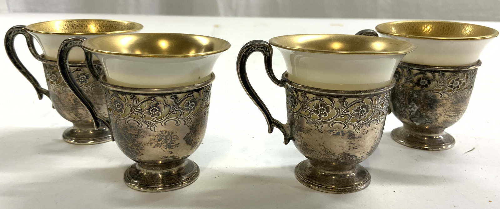 STERLING SILVER & LENOX Porc Set 4 Demitasse: Undersides of demitasse holders are inscribed STERLING 7990. Underside of porcelain vessels are marked LENOX. Porcelain vessels are each cream toned with gilt rims. Sterling silver holders have etched