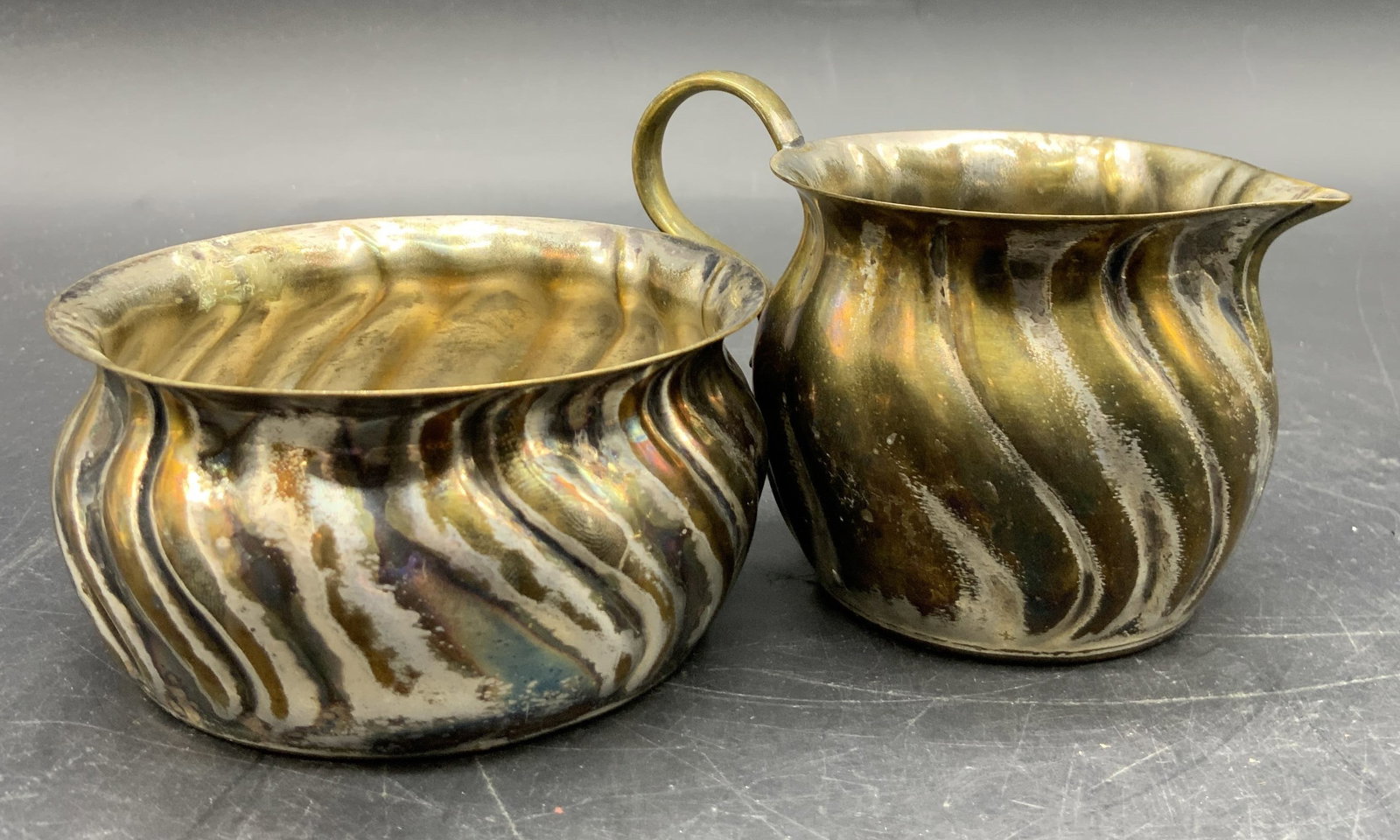 Set PRIMA NS Silver Plate Sugar Bowl & Creamer: A set consisting of a PRIMA NS silver plated sugar bowl and creamer. Marked on underside. Ribbed detail with brass hued accents along the silver plate. Sugar bowl measures approx. 1.75H x 3.5W in. Som
