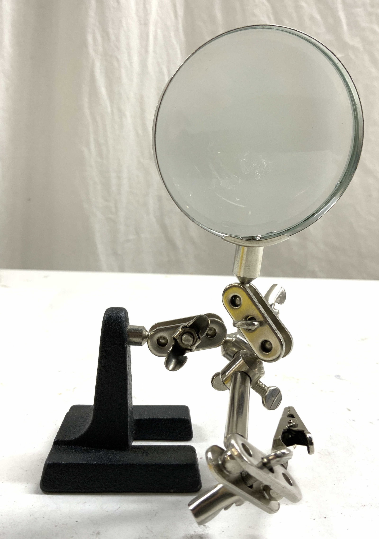 Articulated Jointed Desktop Magnifying Glass: Magnifying glass has multiple adjustable arms. Piece has black toned iron base. Magnifying glass is metal. Height varies by adjustment. Circular Glass area measures approximately 2.5 inches diameter. 