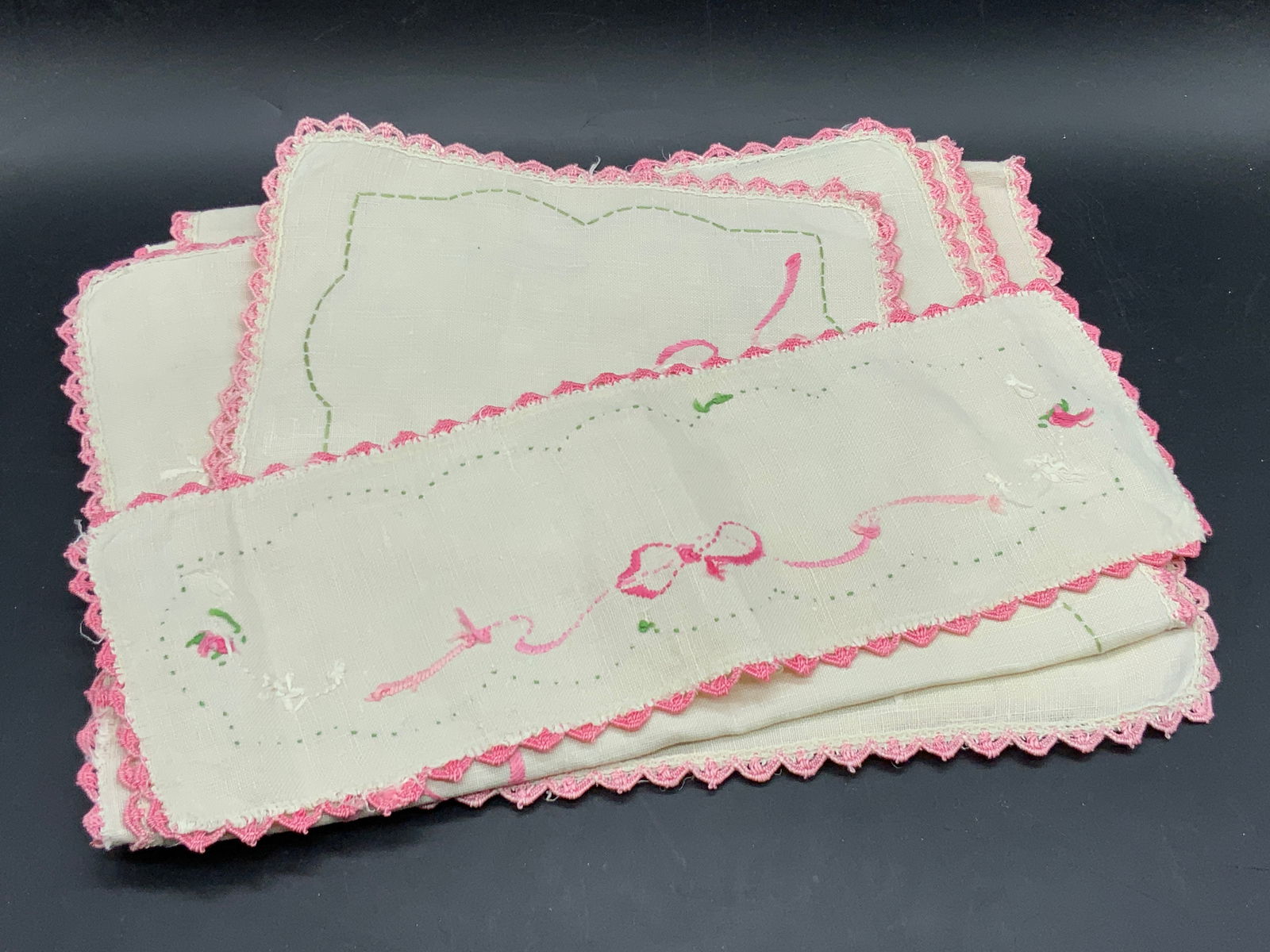 Lot 5 Vtg Embroidered Table Linens, Napkins & More: A lot of five vintage table linens. Lot includes napkins and table accessories. Napkins include basket, ribbon, and floral motifs. Pink, green, and white hues throughout. Largest Measures approx. 40.5