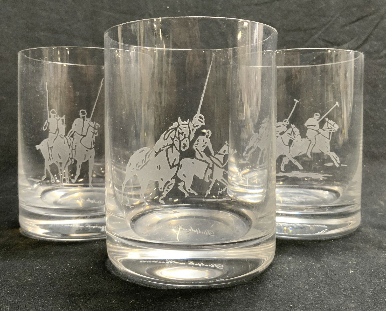 RALPH LAUREN 3 Crystal Lowball Cocktail Glasses: Undersides are signed RAPLH LAUREN. Each are crystal. Lowball glasses each have frosted Ralph Lauren logo on front sides depicting polo players on horseback. Each vessel measures approximately 4.25 in