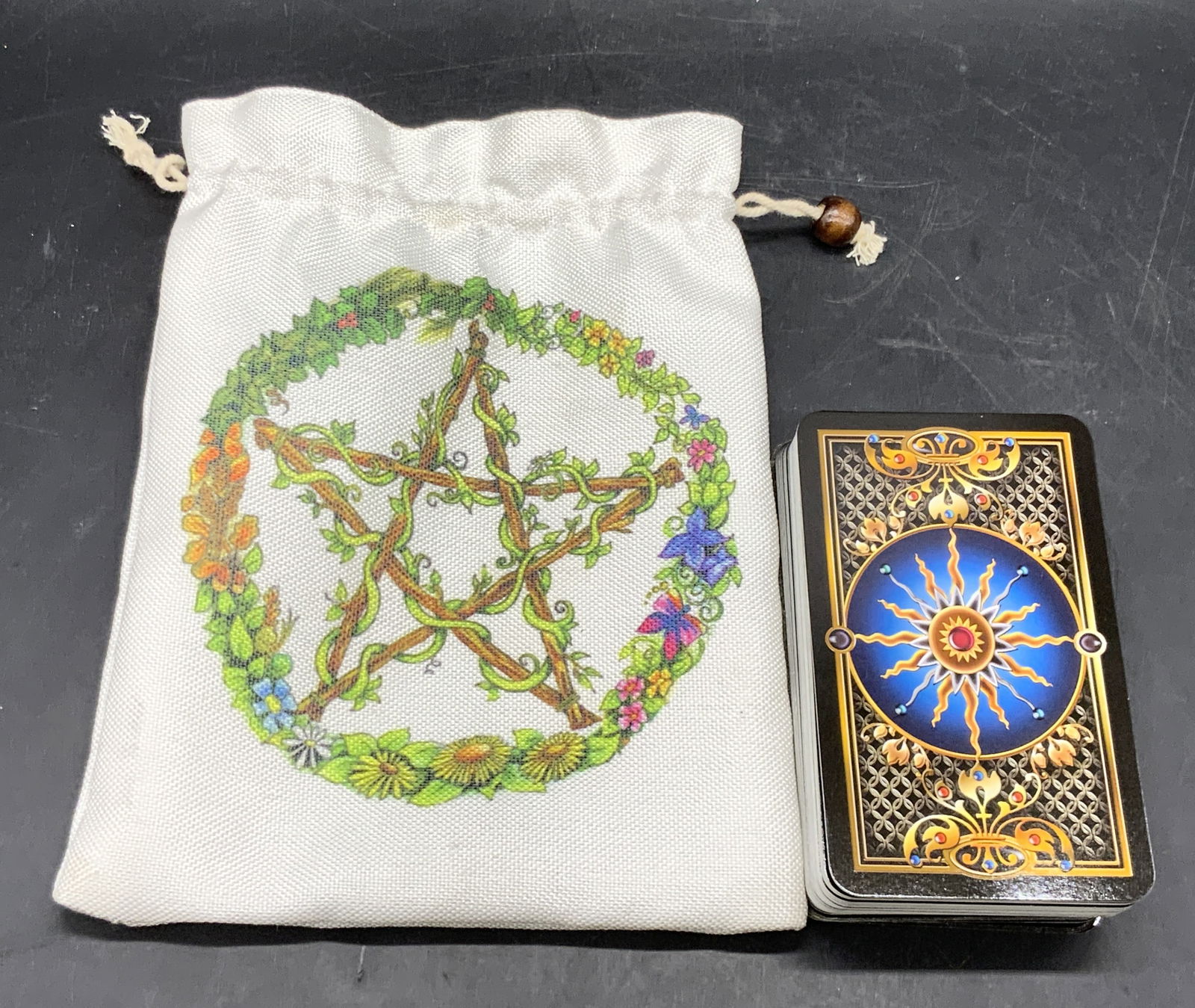 Tarot Cards W/ Drawstring Case: A set of tarot cards contained in a fabric drawstring case. Floral pentagram motif to the case. Cards measure approx. 4.75L x 2.75W in. Some may be missing from deck. One bead needs reattachment. Some