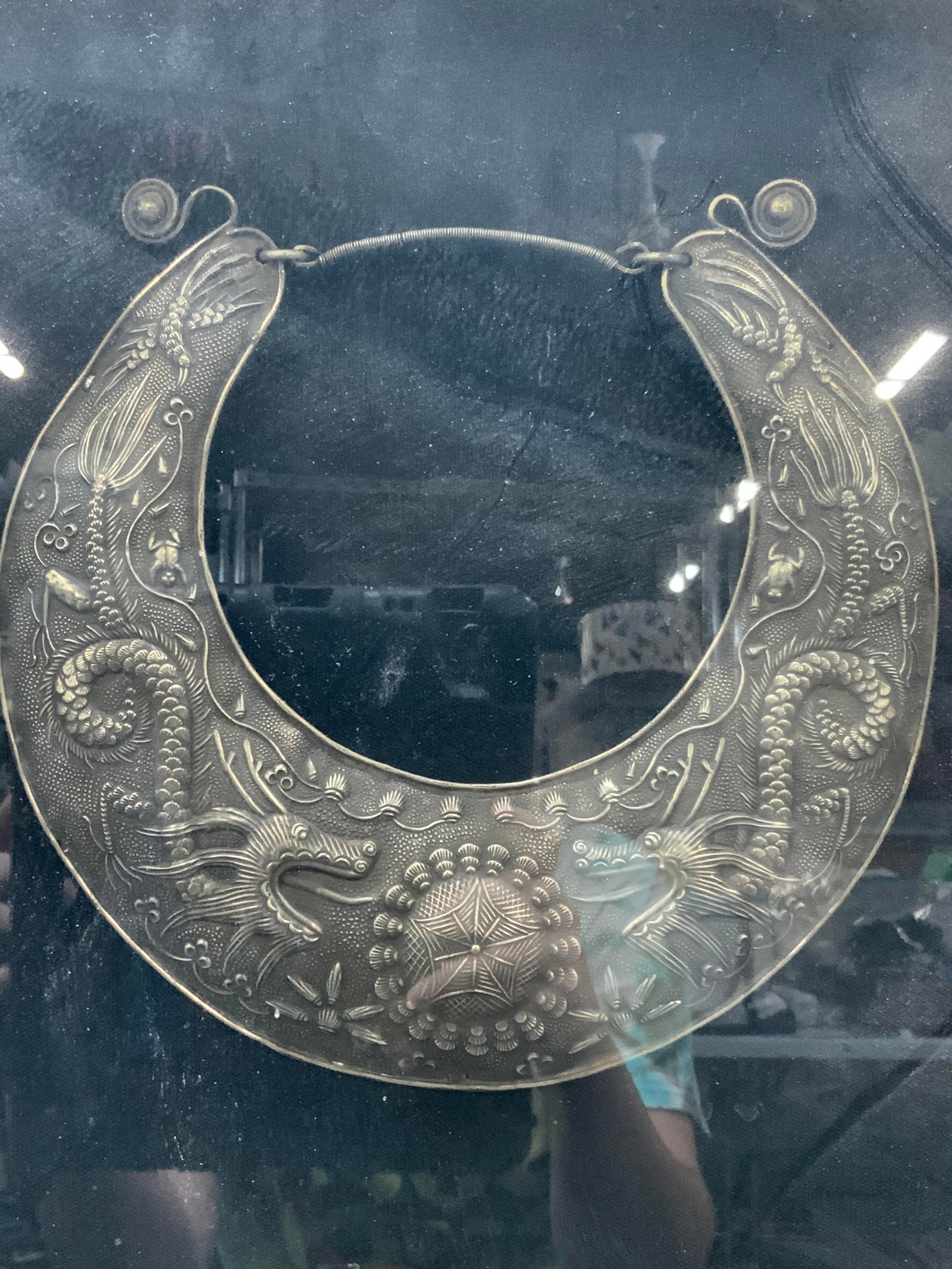Silver Plate Miao Ceremonial Dragon Necklace: Marked on backside, silver plate replica of ceremonial necklace, from the Miao people. Embossed with images of dragons and floral motifs. Mounted with in a silver leafed wooden frame with linen mattin